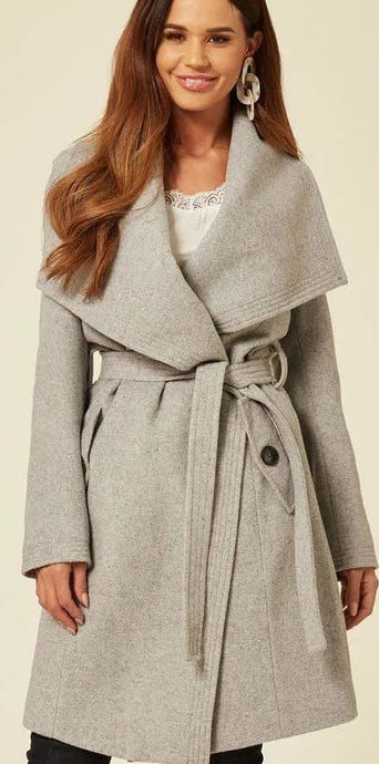 Woman wearing a gray coat with a belt, standing against a plain background.