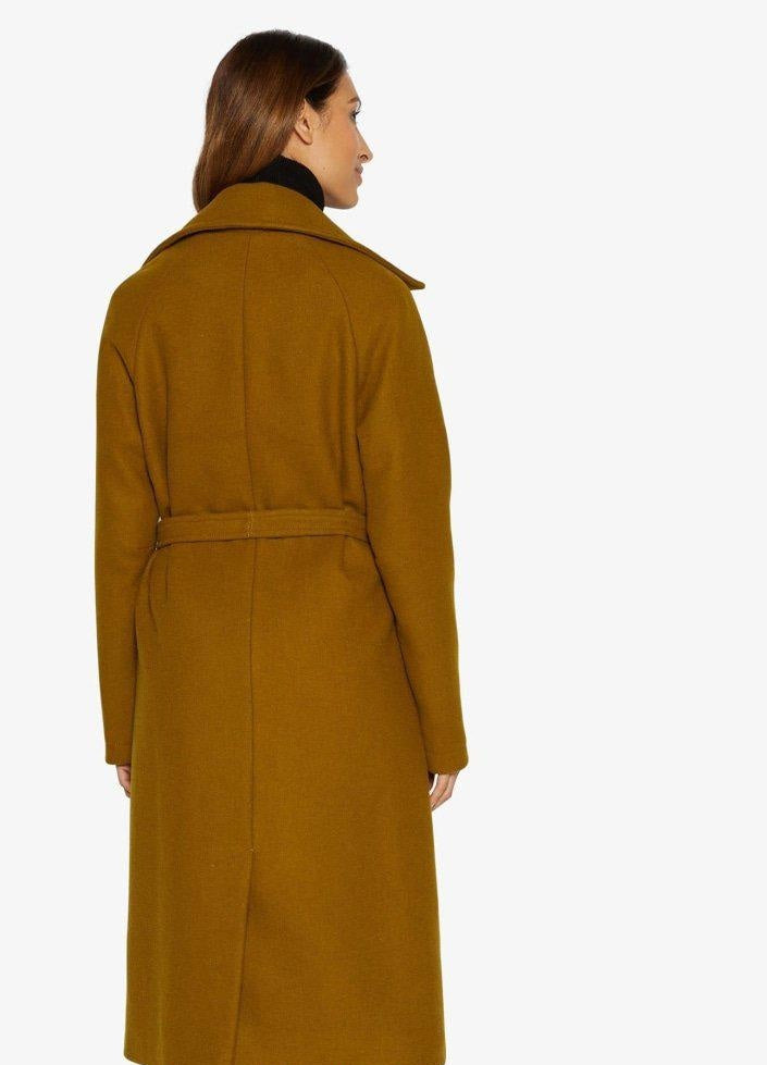 Woman wearing a long mustard yellow coat on a white background