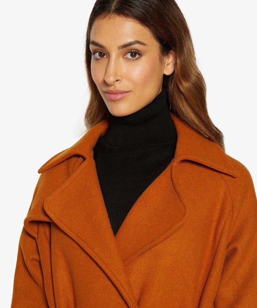 Woman wearing a brown coat over a black turtleneck on a white background
