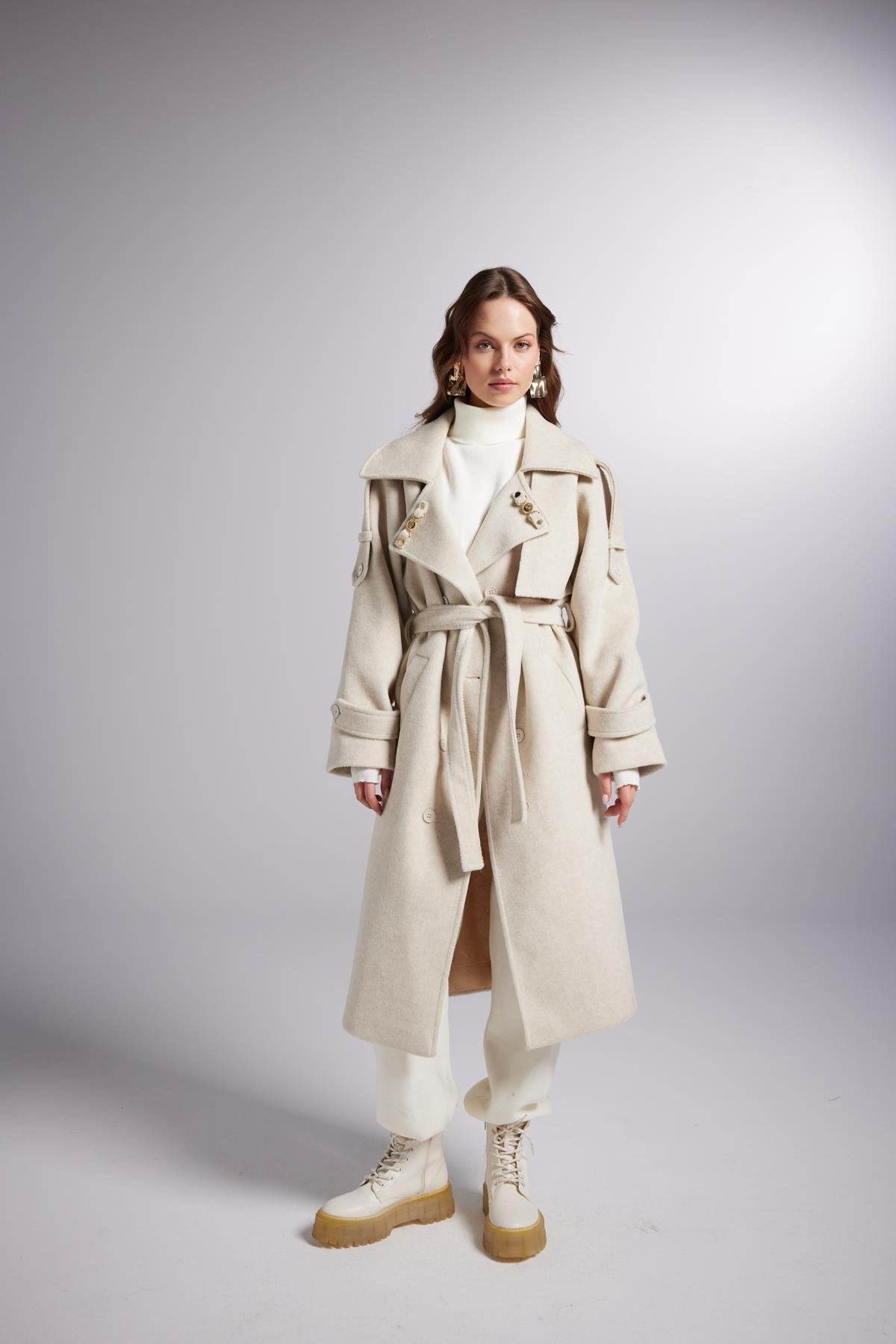 Woman wearing a long beige trench coat on a gray background