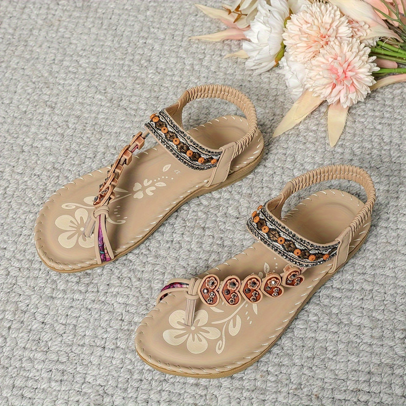 Beige sandals with decorative straps on a textured surface with flowers.