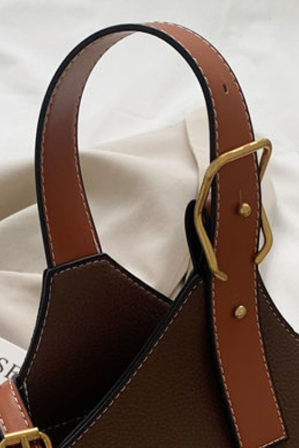 Close-up of a brown leather handbag with a gold buckle on a white background
