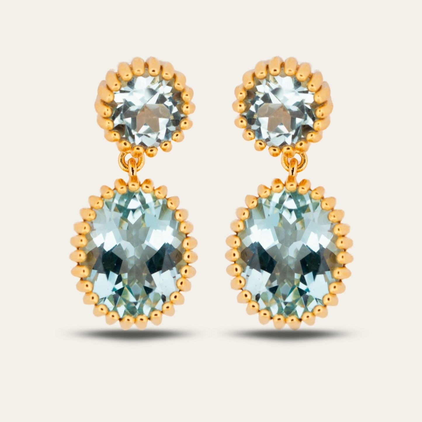 Gold earrings with clear gemstones on a light beige background