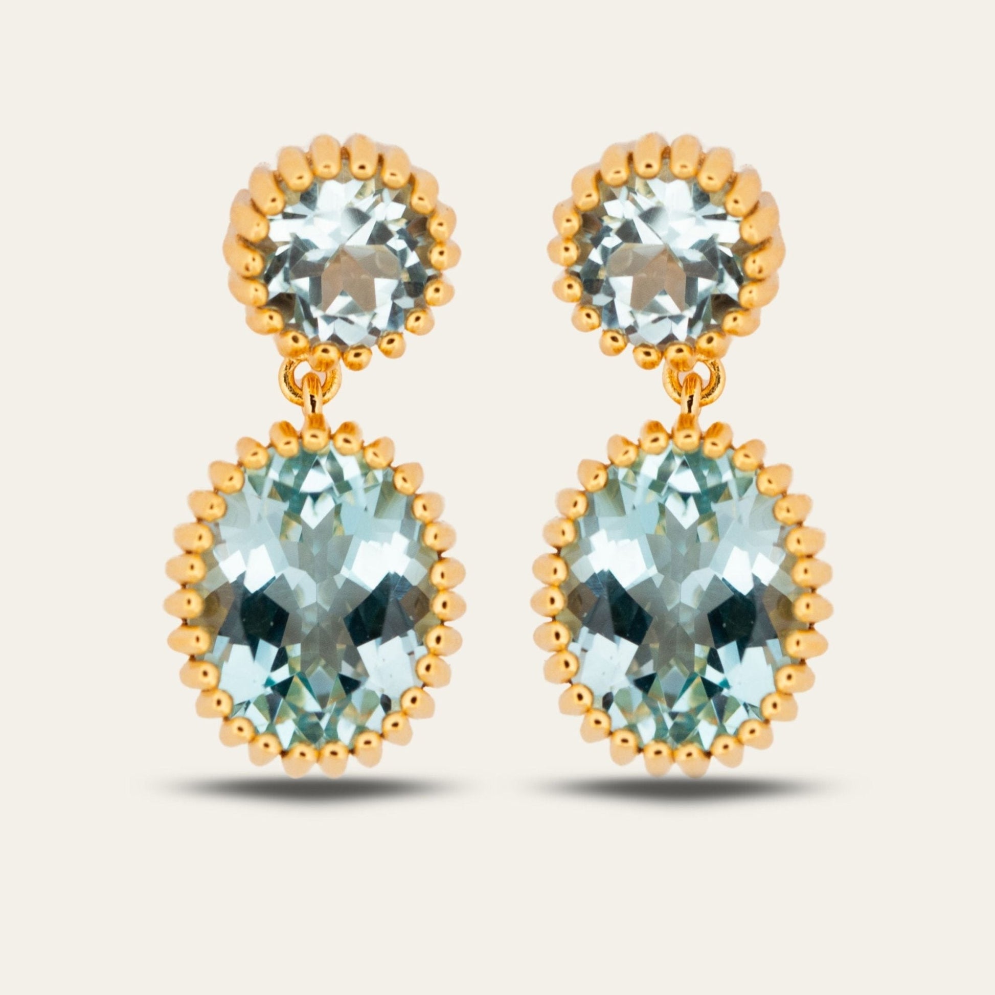 Gold earrings with clear gemstones on a light beige background