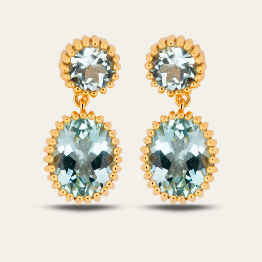 Gold earrings with clear gemstones on a light beige background