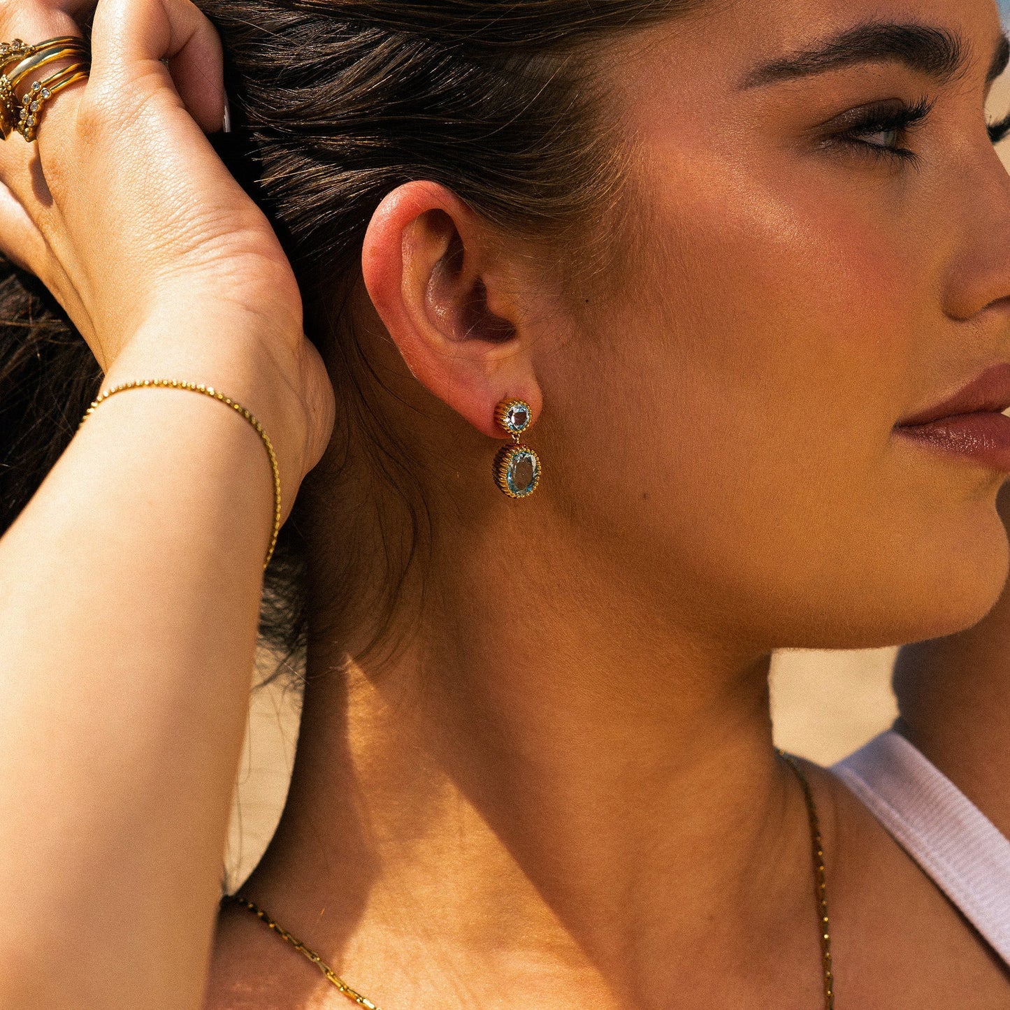 Close-up of a woman wearing gold earrings and jewelry, with a blurred background.