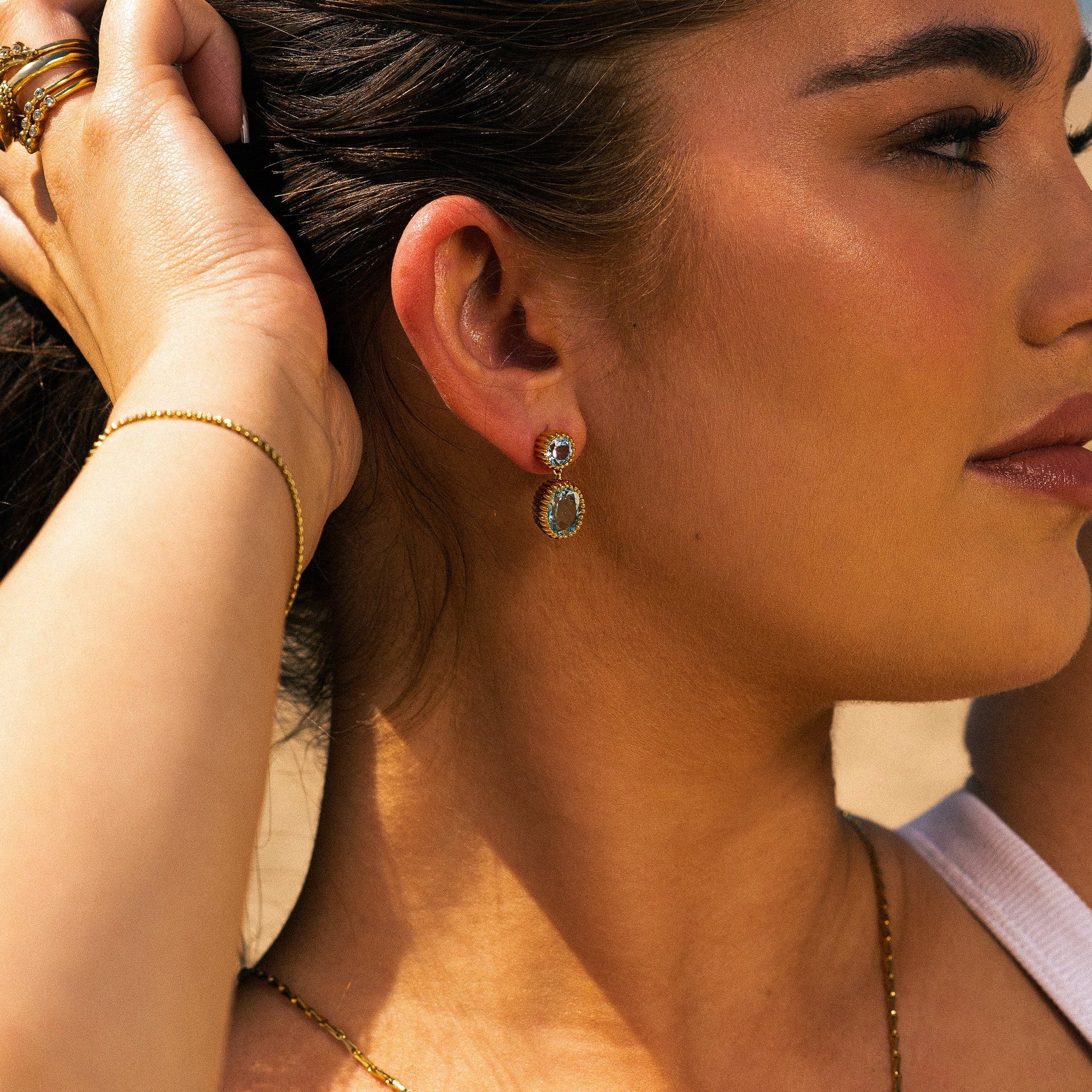 Close-up of a woman wearing gold earrings and jewelry, with a blurred background.