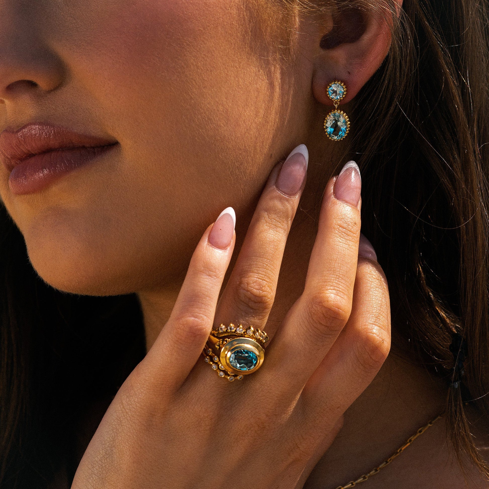 Close-up of a woman wearing gold ring and earrings with blue gemstones.