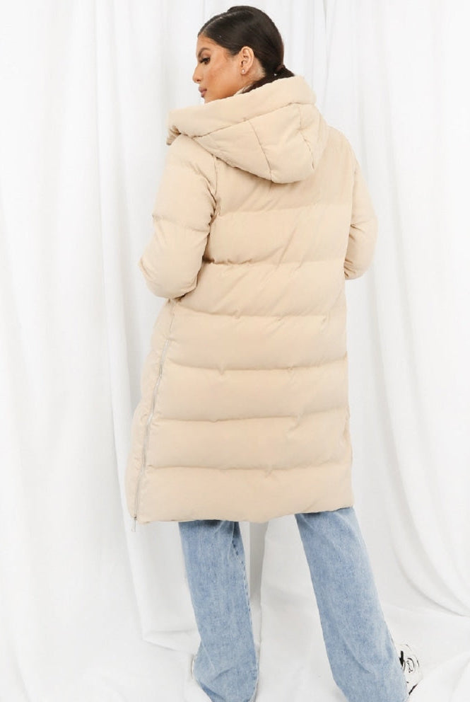 Person wearing a long beige puffer coat against a white background
