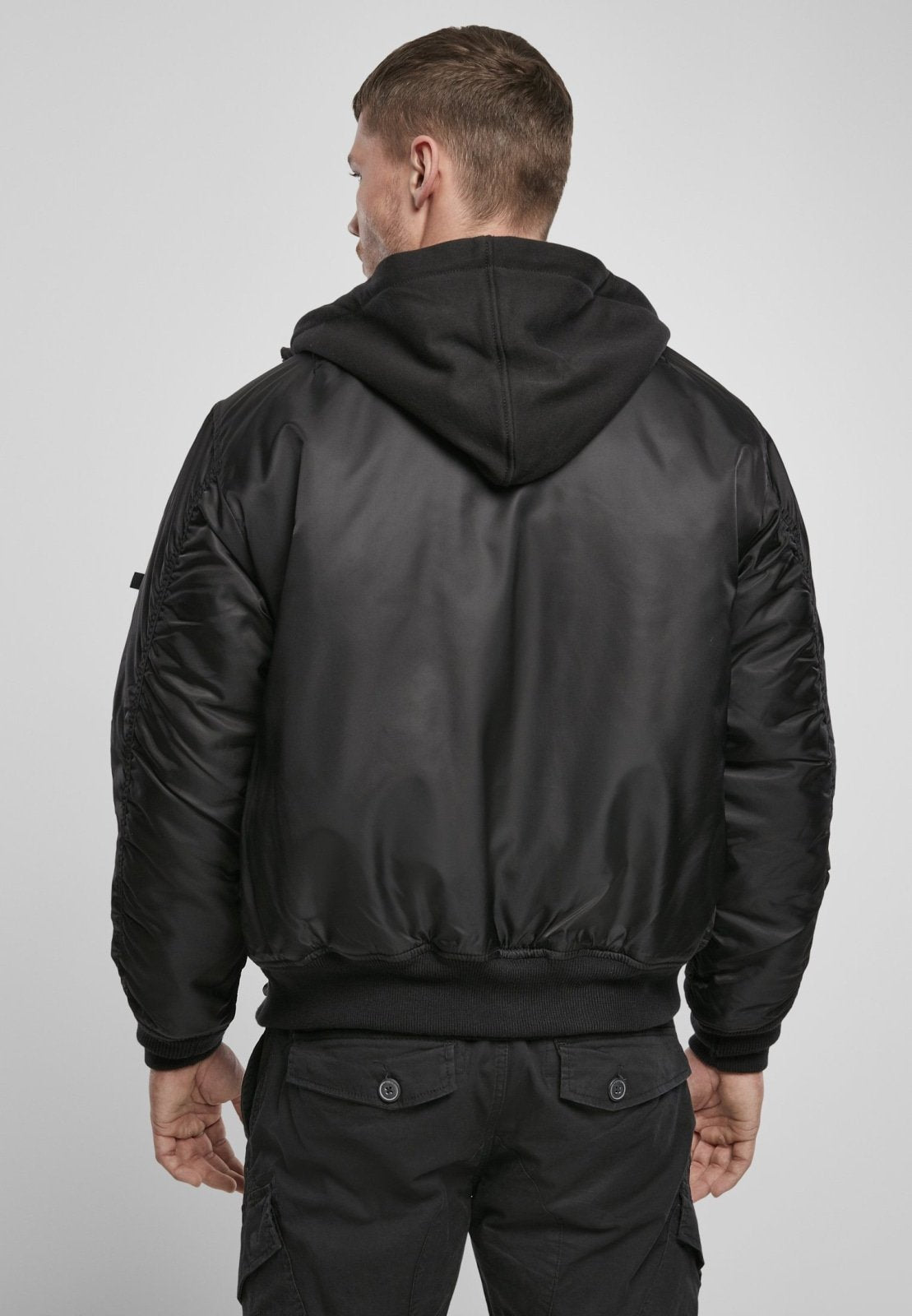 Man wearing a black bomber jacket with a hood on a plain background