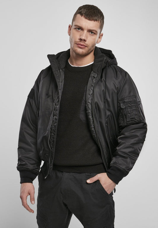 Man wearing a black bomber jacket over a black sweater on a light gray background