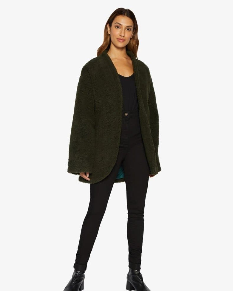 Woman wearing a green coat over a black outfit on a white background