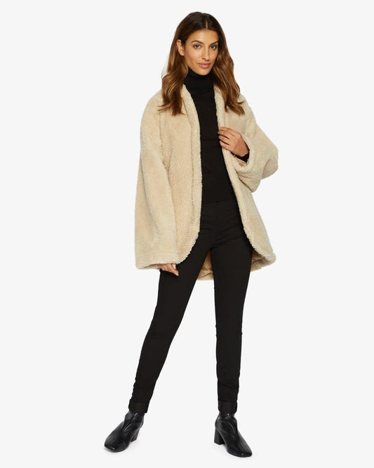 Woman wearing a beige coat over a black outfit on a white background