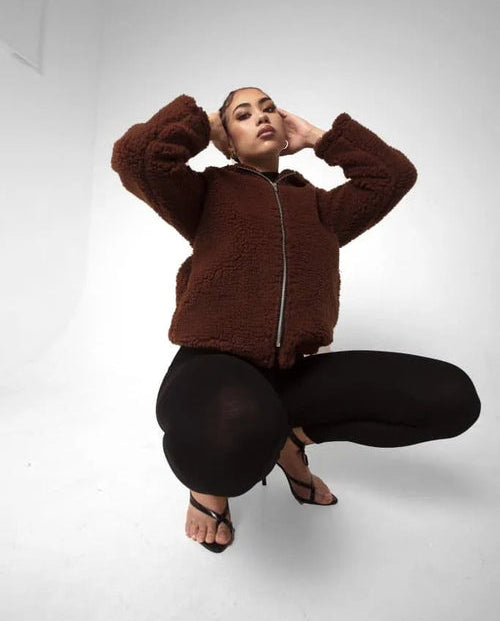 Woman wearing a brown fleece jacket and black pants on a white background