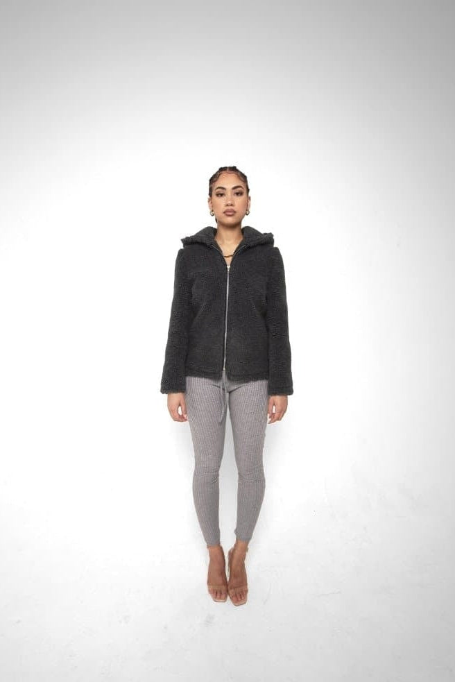 Person wearing a black hoodie and gray leggings on a white background