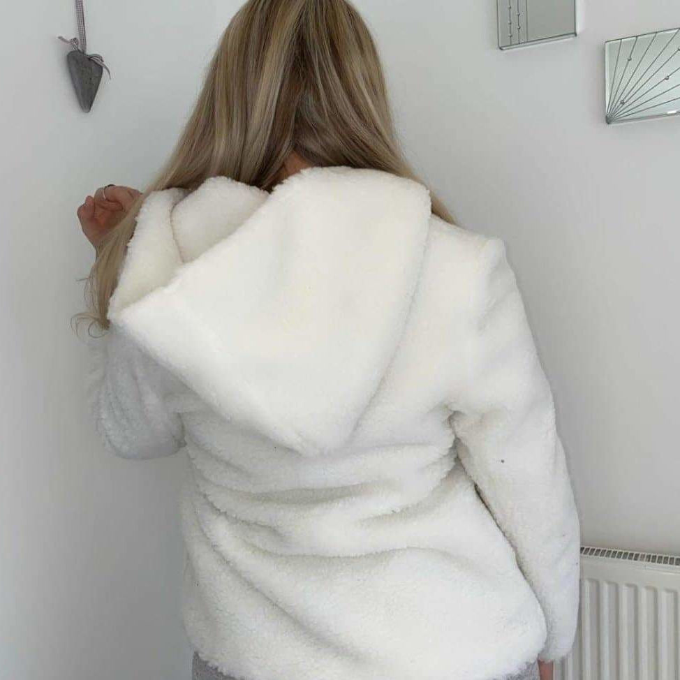 Person wearing a white fur coat with a hood in a room.