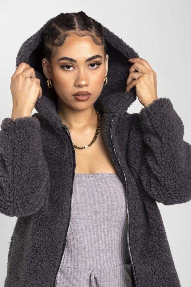 Woman wearing a dark gray fluffy hooded coat on a white background