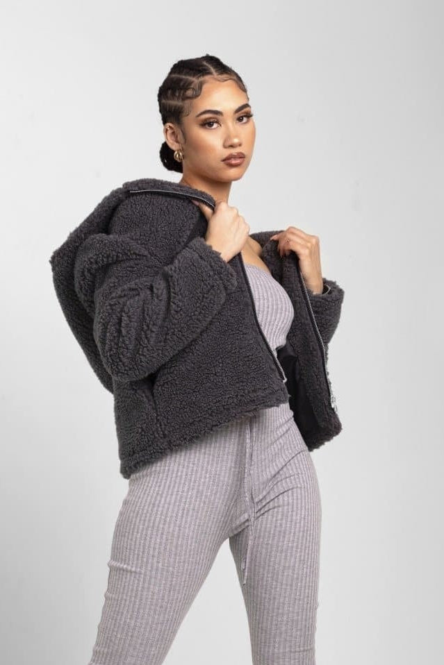 Woman wearing a dark gray textured jacket over a light gray outfit on a white background