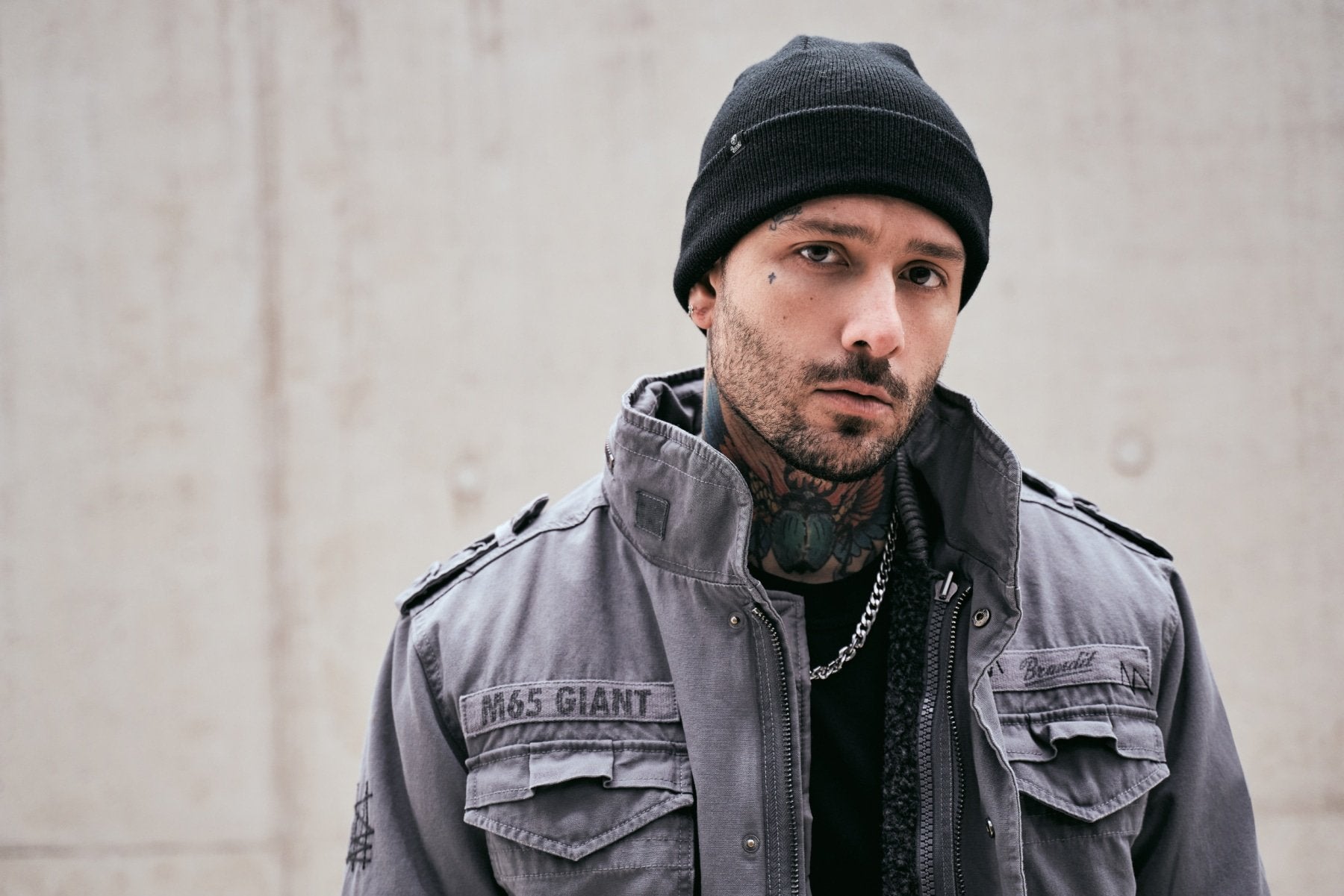 Man wearing a gray jacket and black beanie against a plain background
