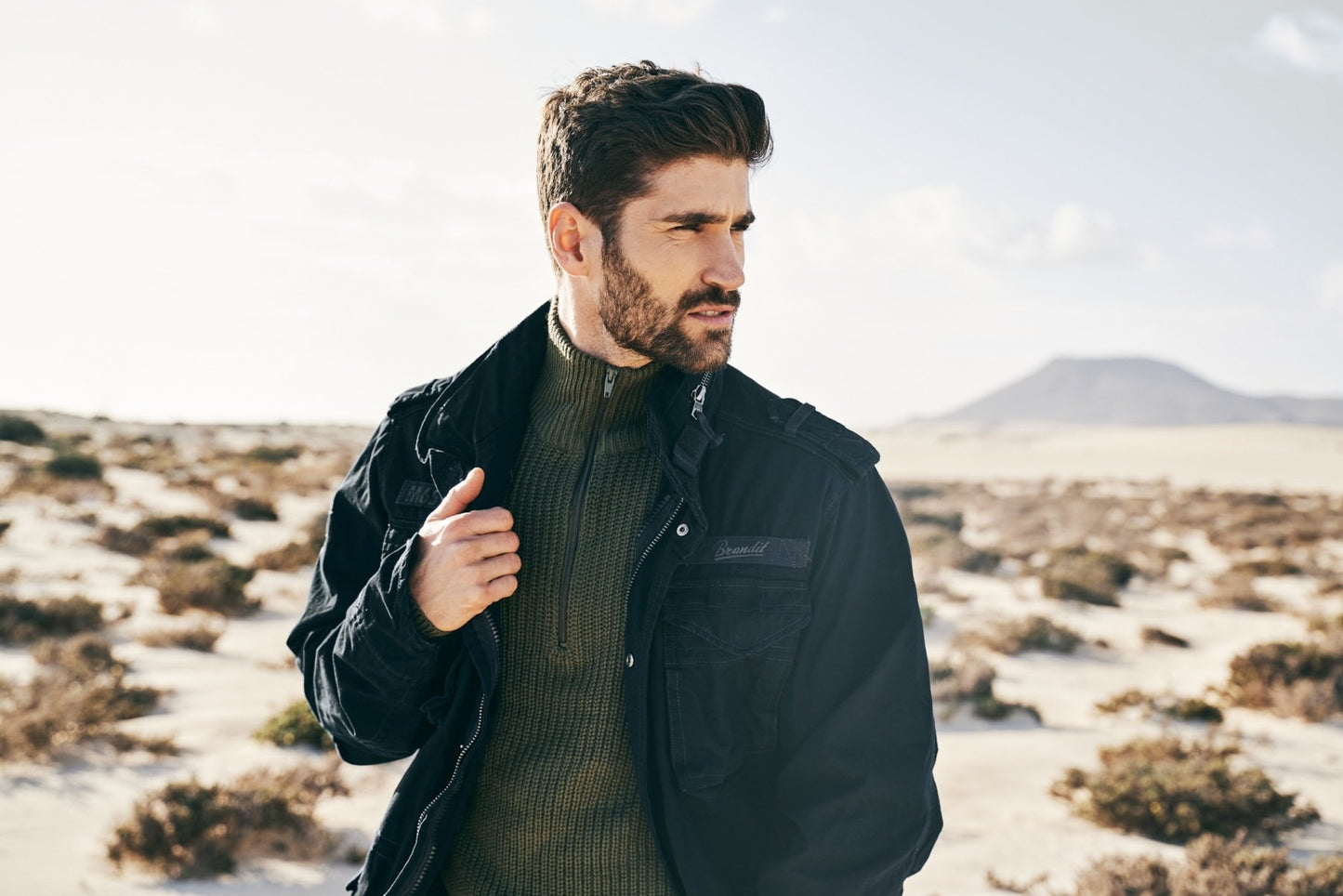 Man wearing a dark jacket and sweater in a desert landscape