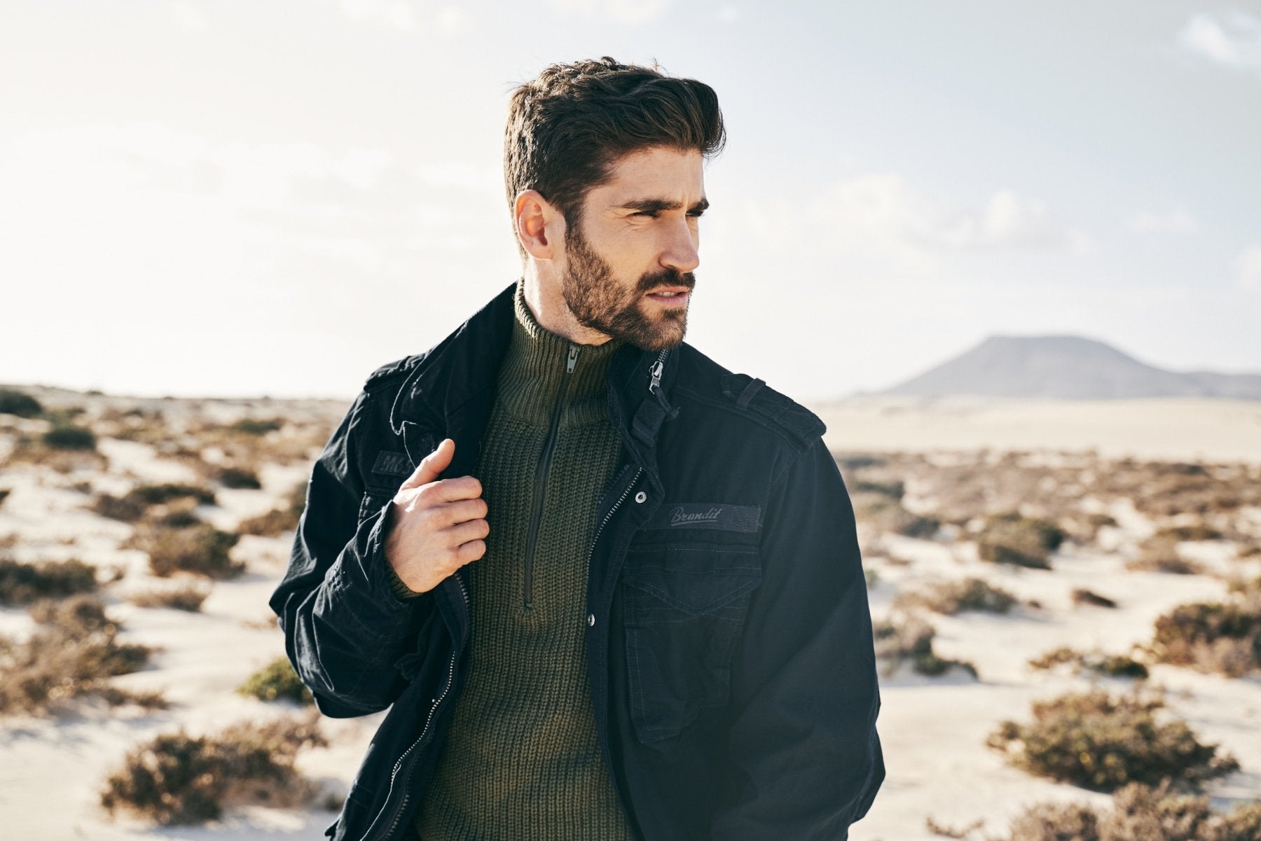 Man wearing a dark jacket and sweater in a desert landscape