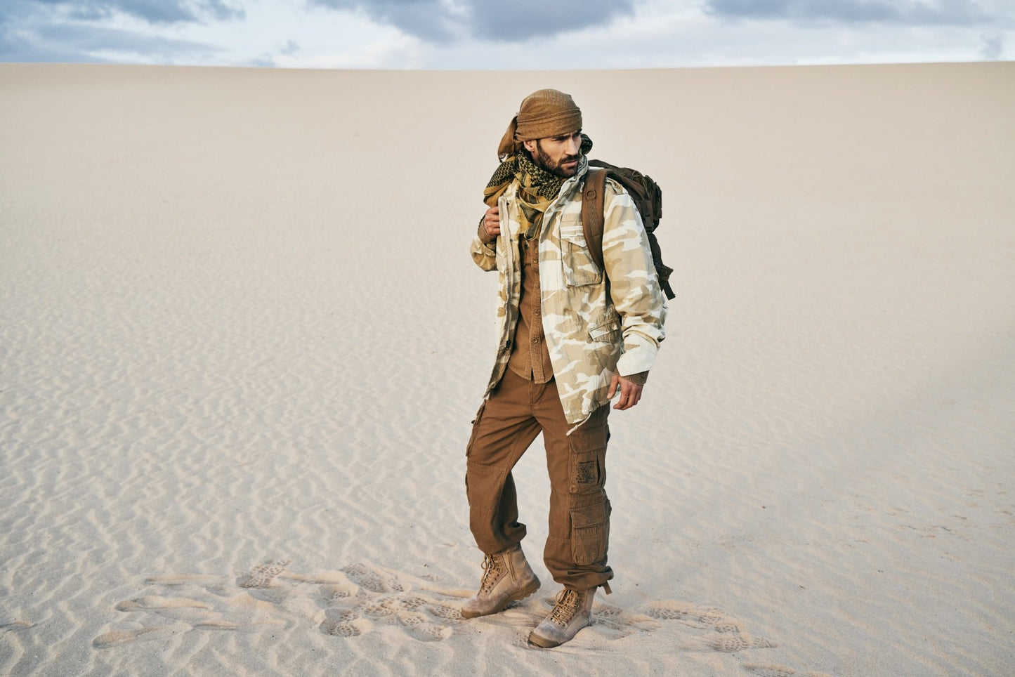 Person in desert attire standing on sand dunes with a backpack