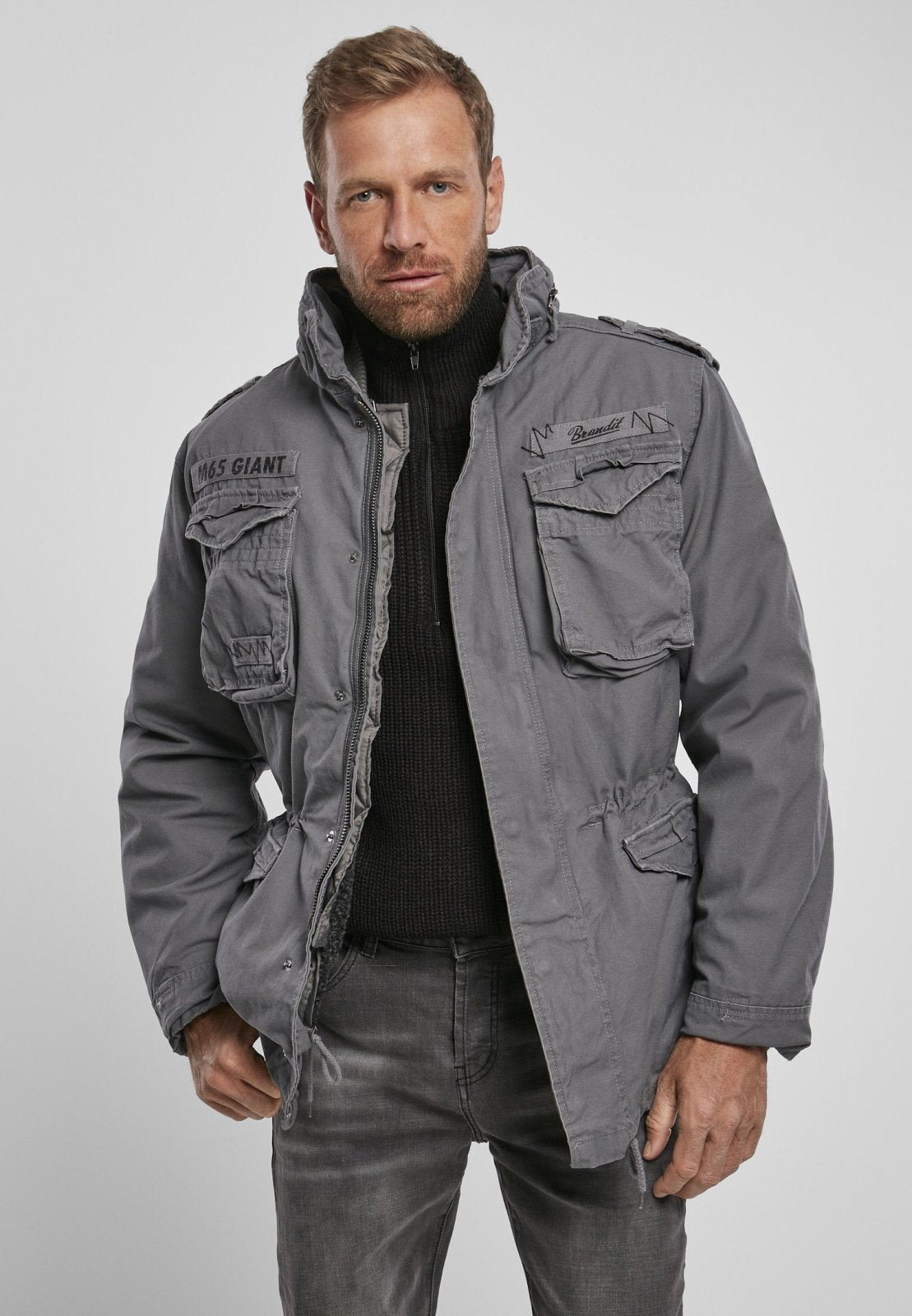 Man wearing a gray jacket with multiple pockets on a plain background