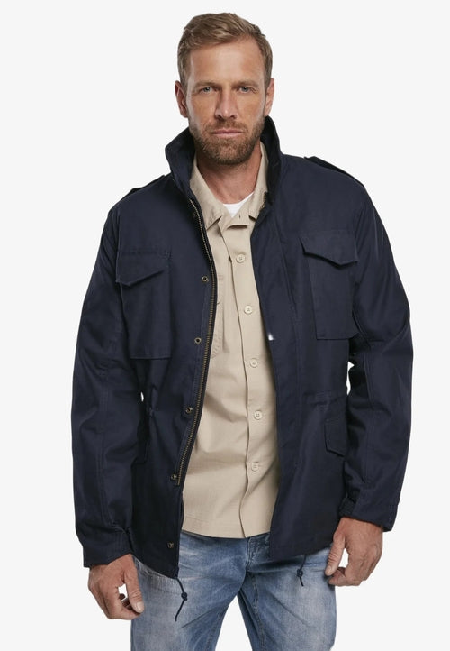 Man wearing a navy jacket over a beige shirt with a white background