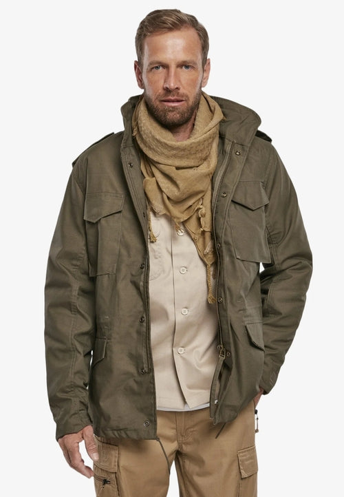 Man wearing a green jacket, beige scarf, and pants on a white background