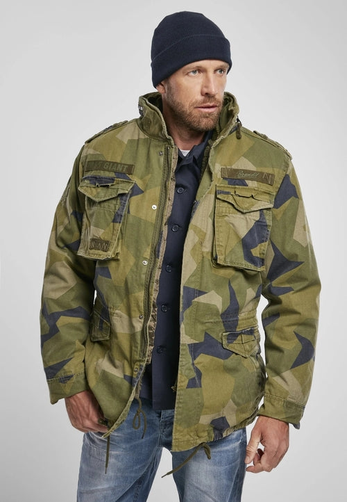 Man wearing a green camouflage jacket and blue beanie on a light gray background