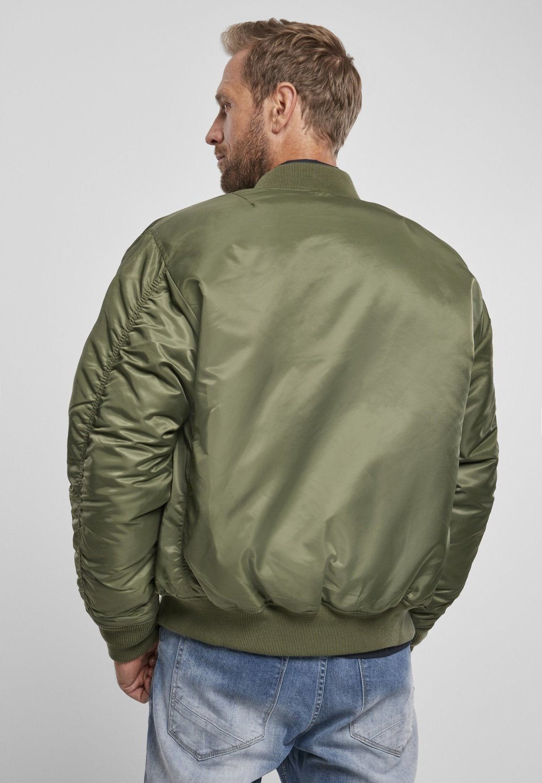 Man wearing a green bomber jacket and blue jeans on a white background