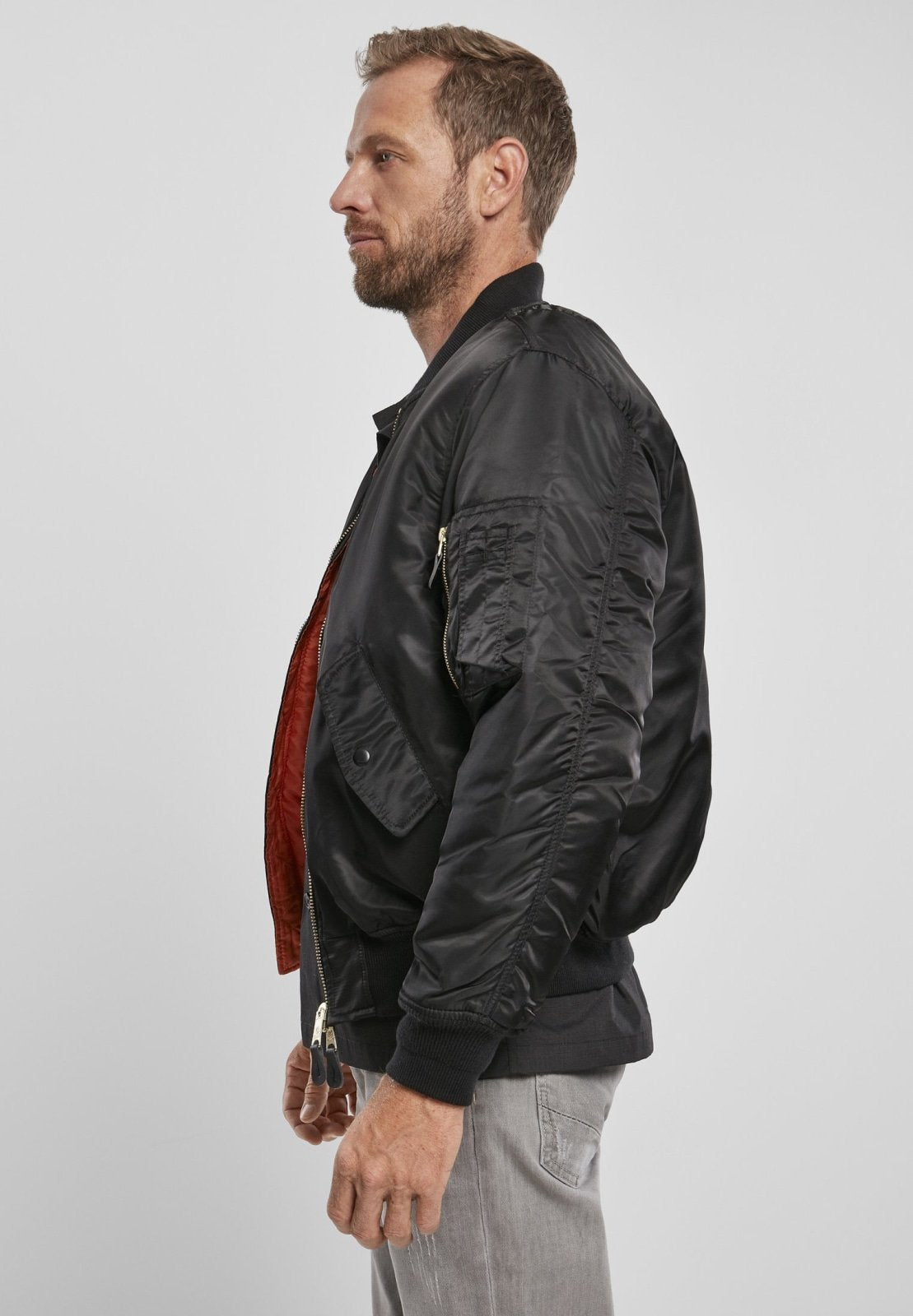 Man wearing a black bomber jacket with a red lining on a light gray background