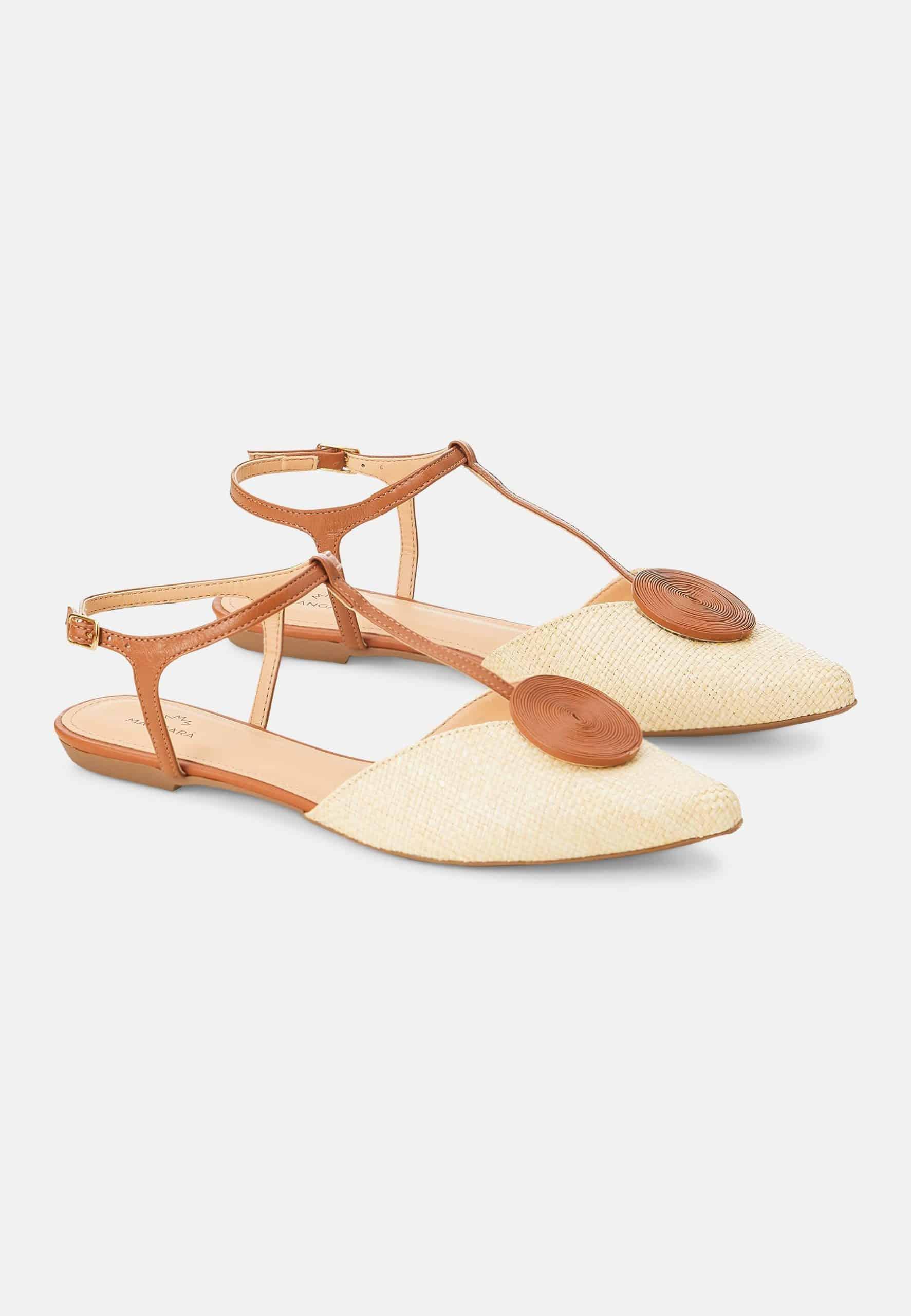 Pair of flat sandals with tan straps and wooden accents on a white background
