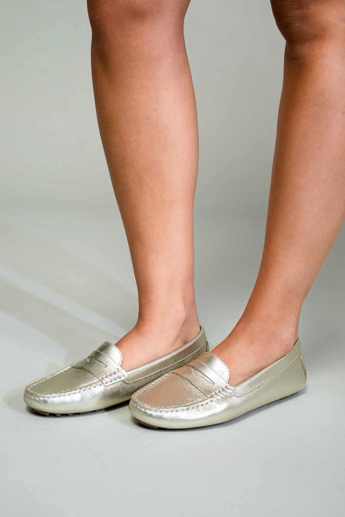 Silver loafers worn by a person on a neutral background