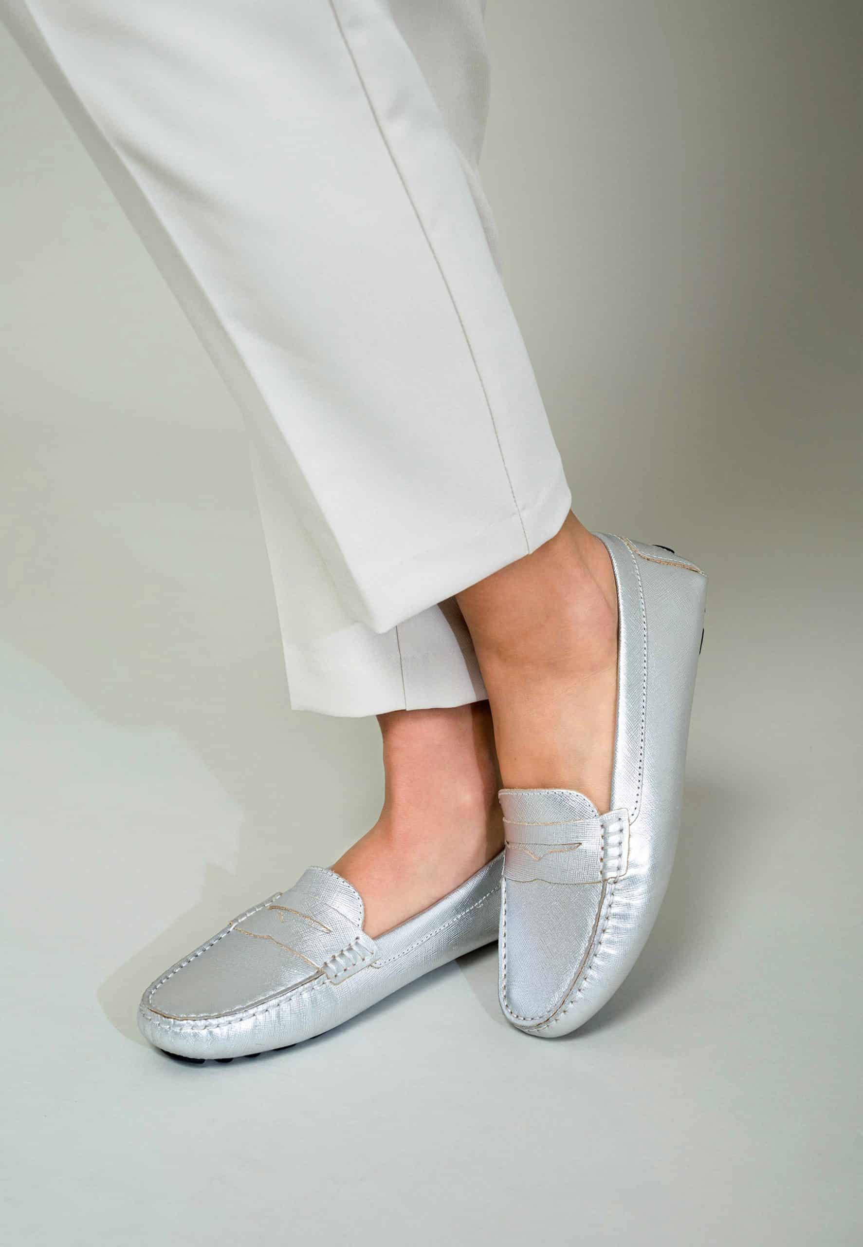 Silver loafers worn with white pants on a light gray background