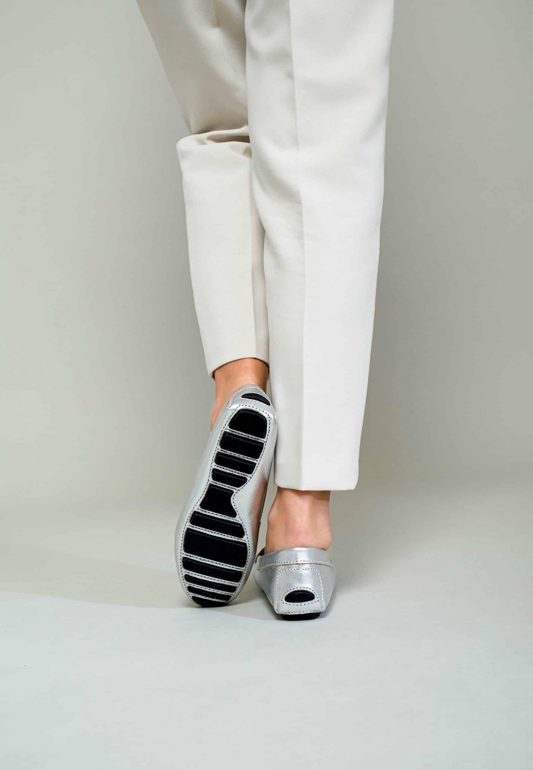 Silver loafers with black sole worn with white pants on a plain background