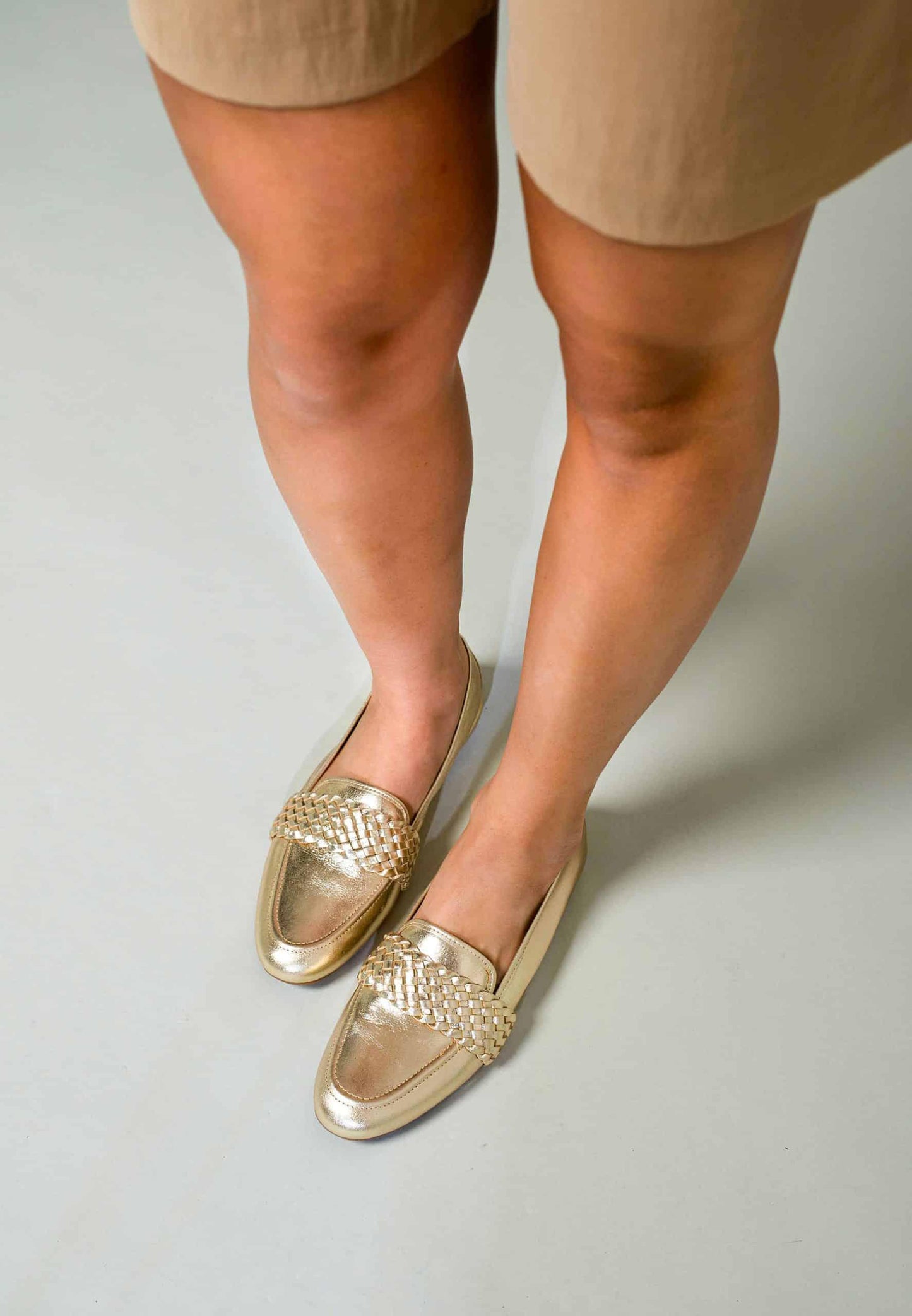 Gold loafers worn with beige shorts on a plain background