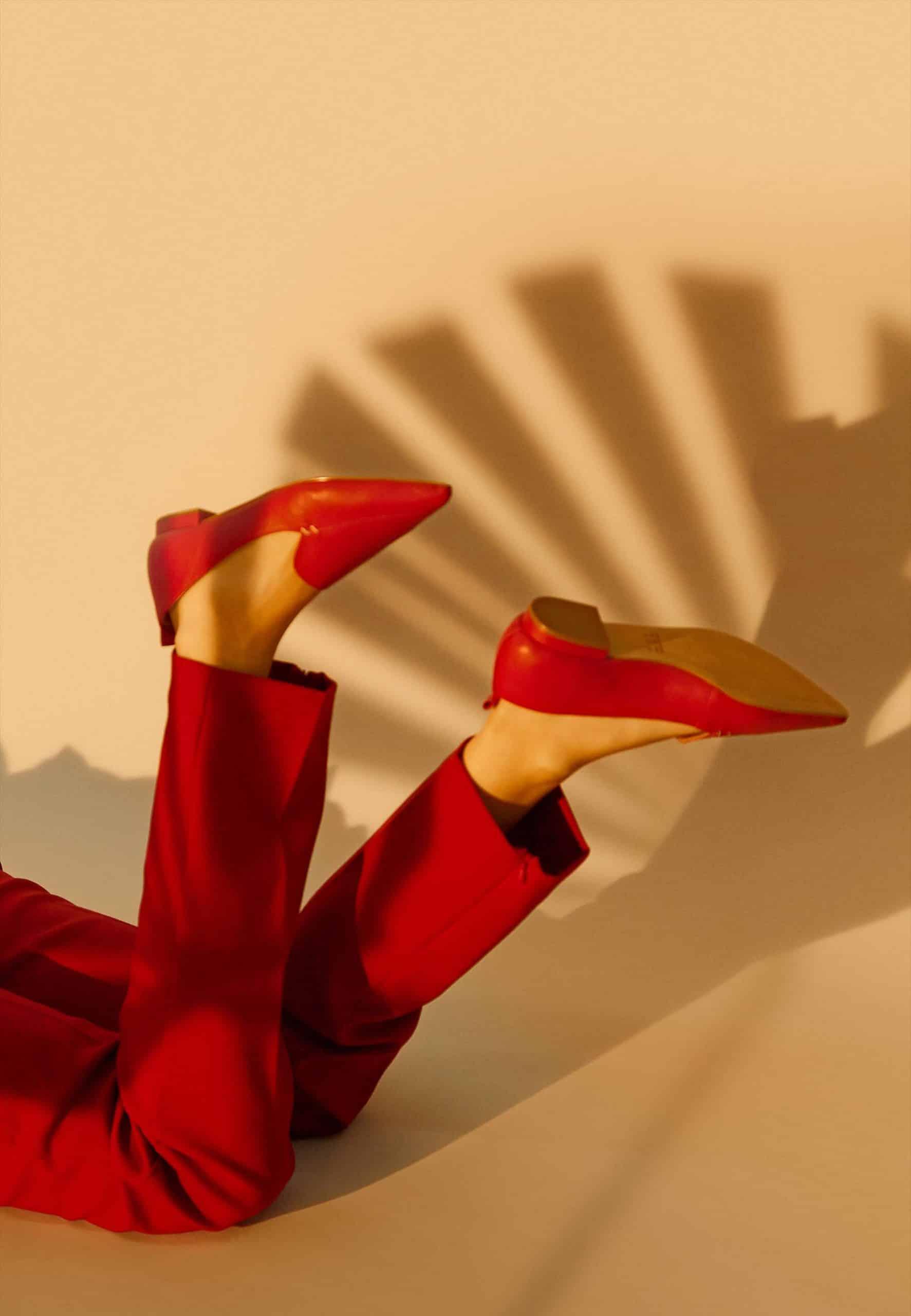 Person wearing red high-heeled shoes and pants against a beige background