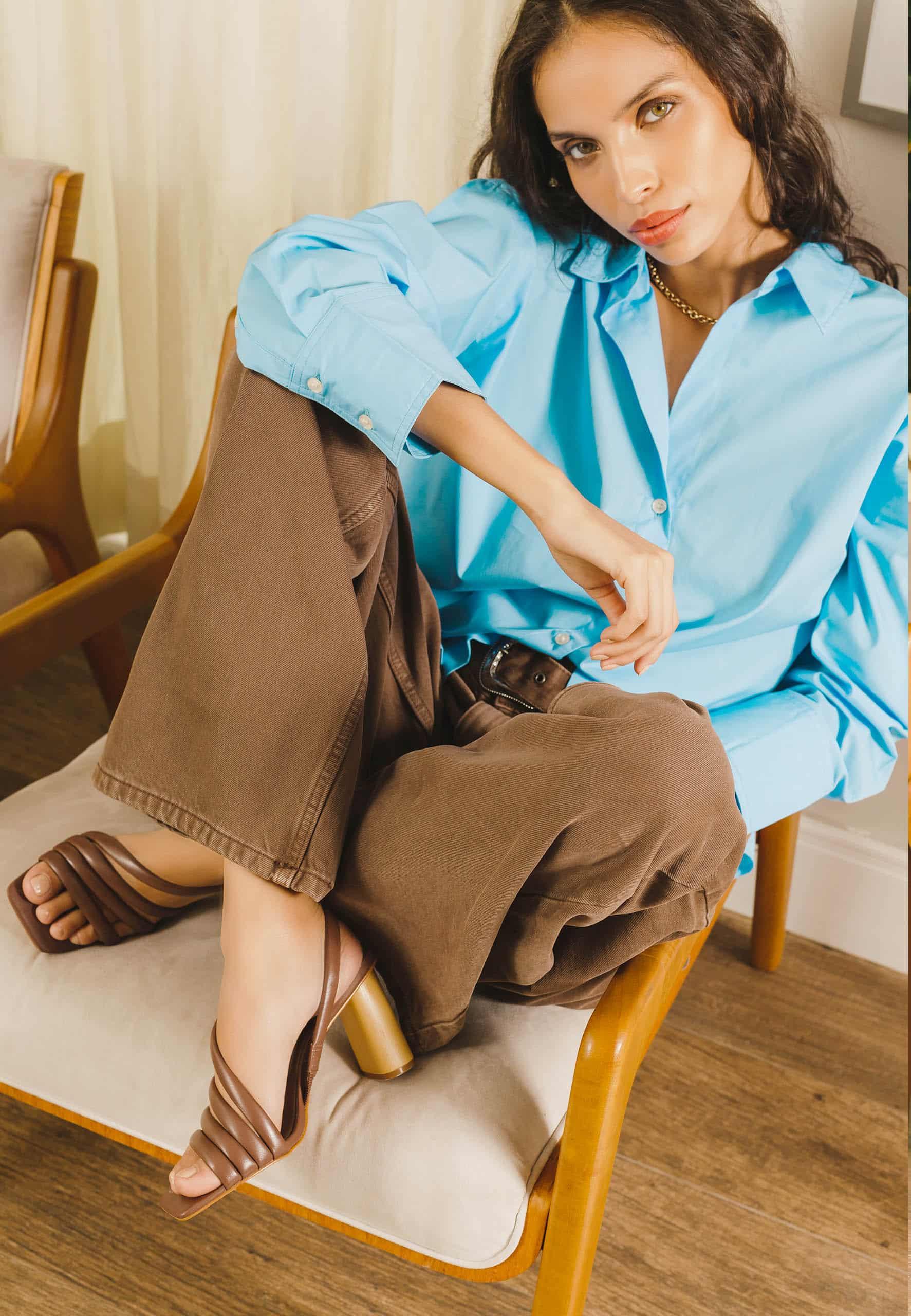 Woman sitting on a chair wearing a light blue shirt and brown pants.