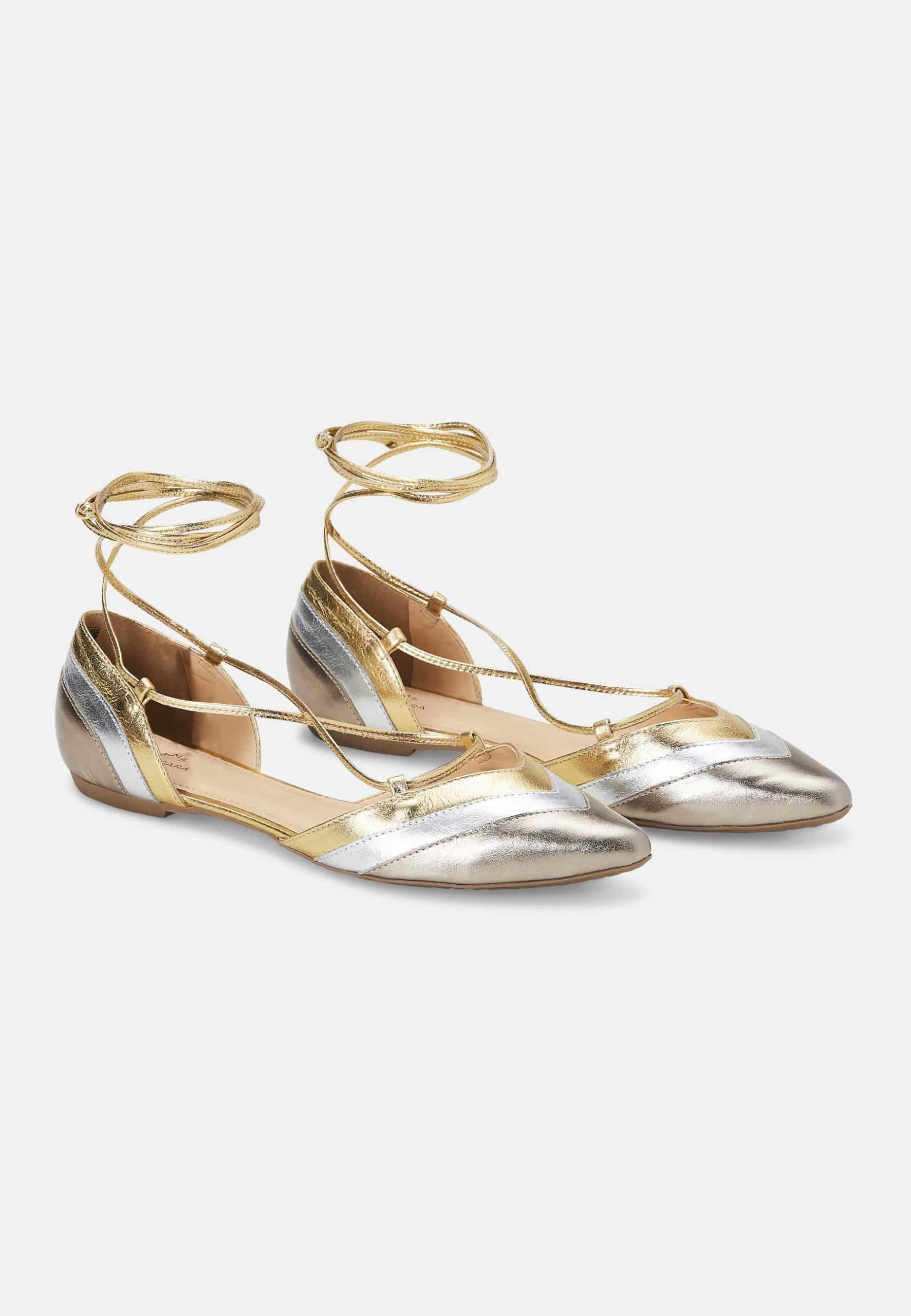 Pair of metallic gold and silver flat shoes with ankle straps on a white background