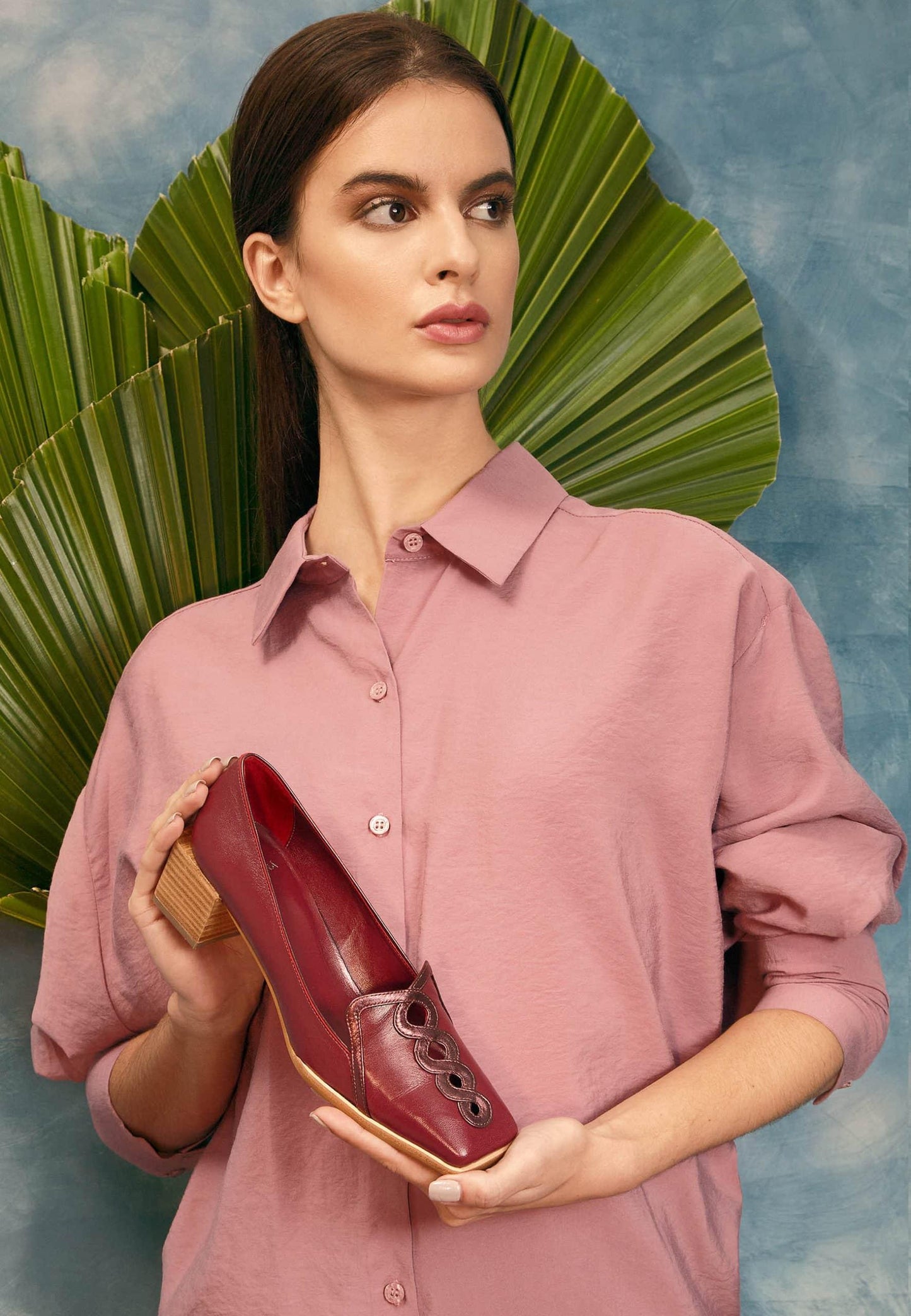 Woman holding a pair of red loafers against a decorative background