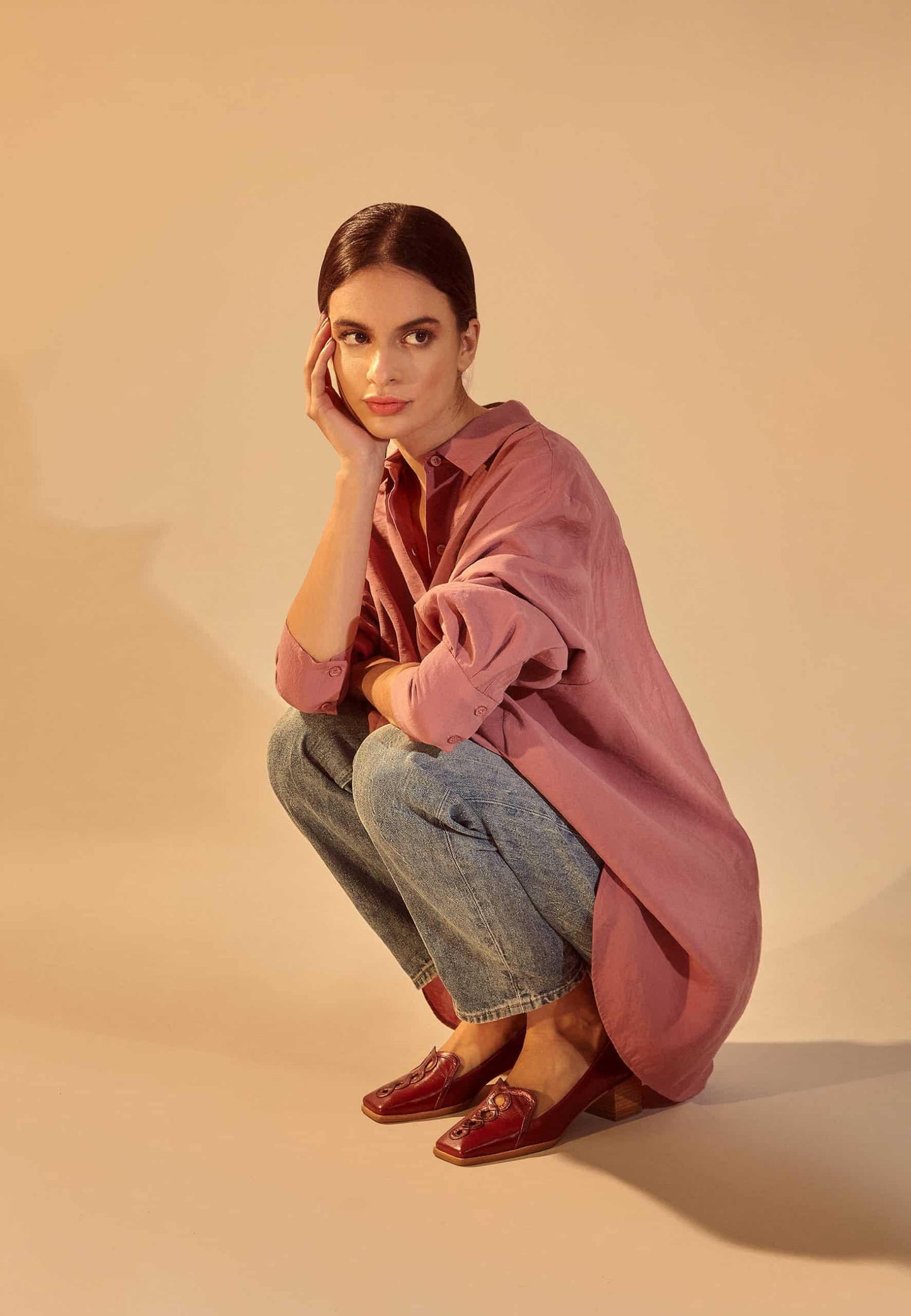 Woman in a pink shirt and jeans sitting on a beige background