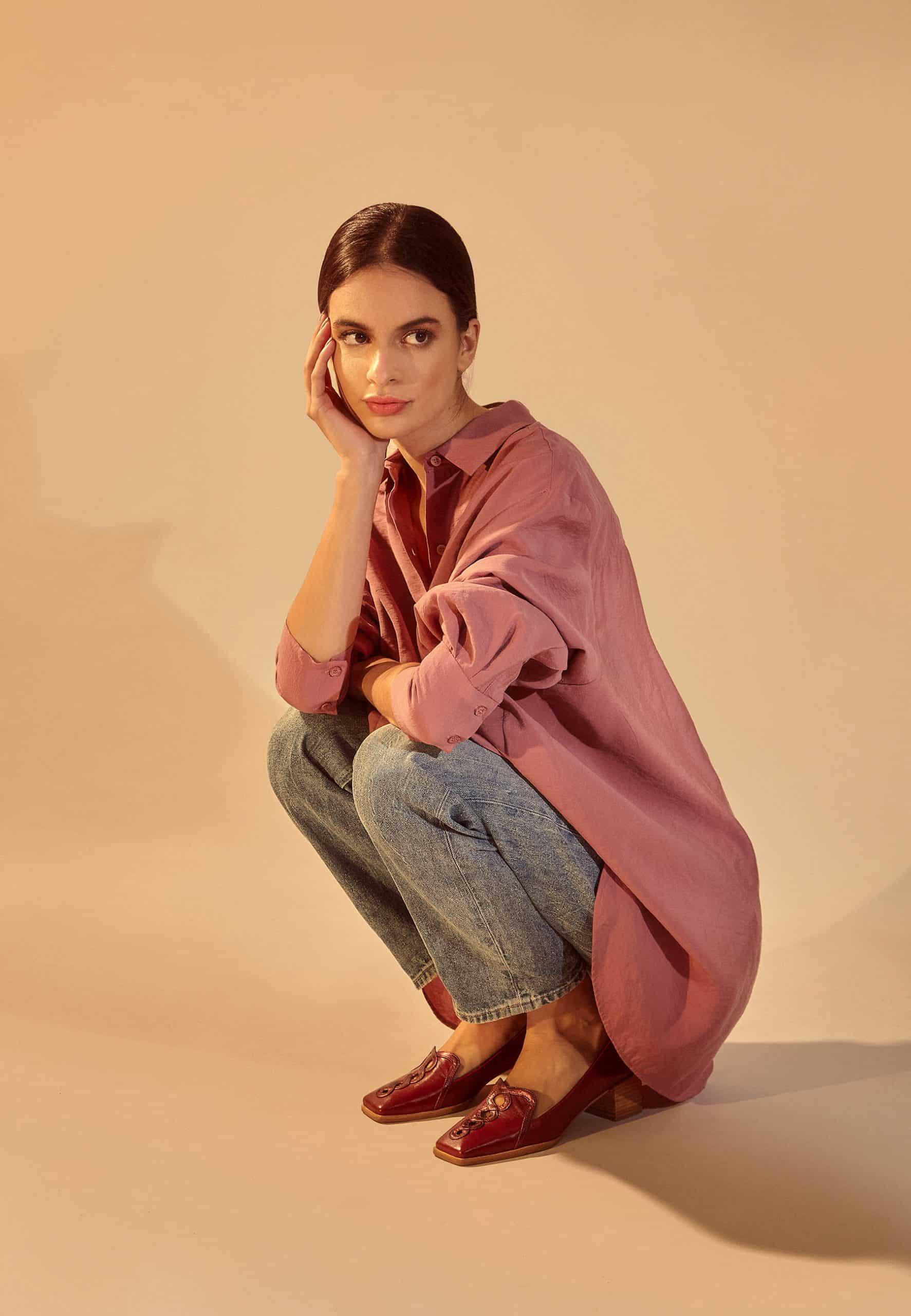 Woman in a pink shirt and jeans sitting on a beige background