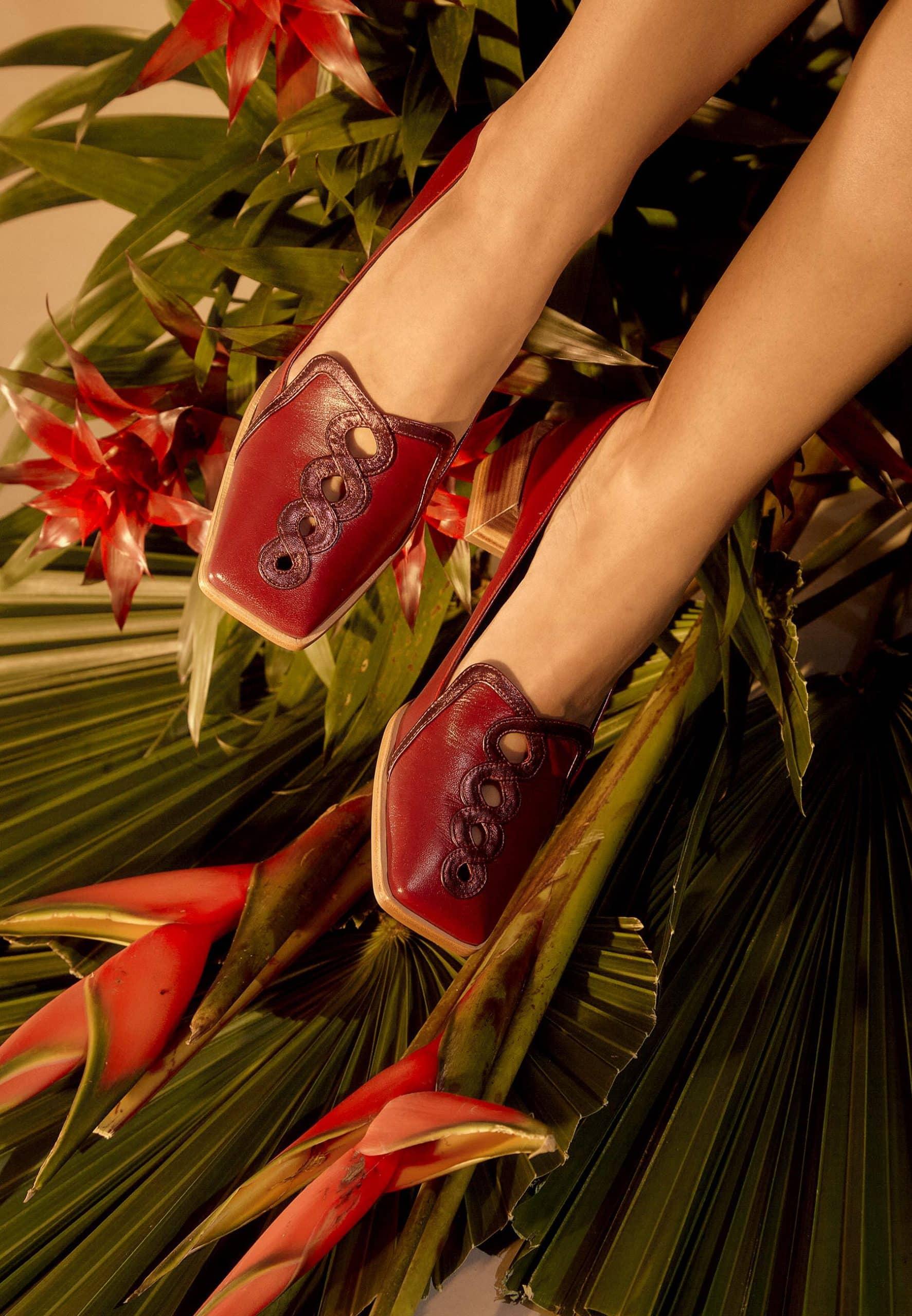 Red loafers with decorative elements on a background of green leaves and red flowers