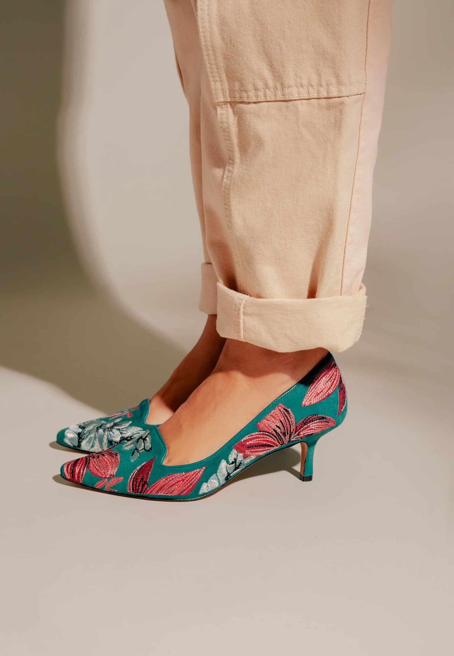 Teal shoes with pink floral pattern worn with beige pants on a neutral background