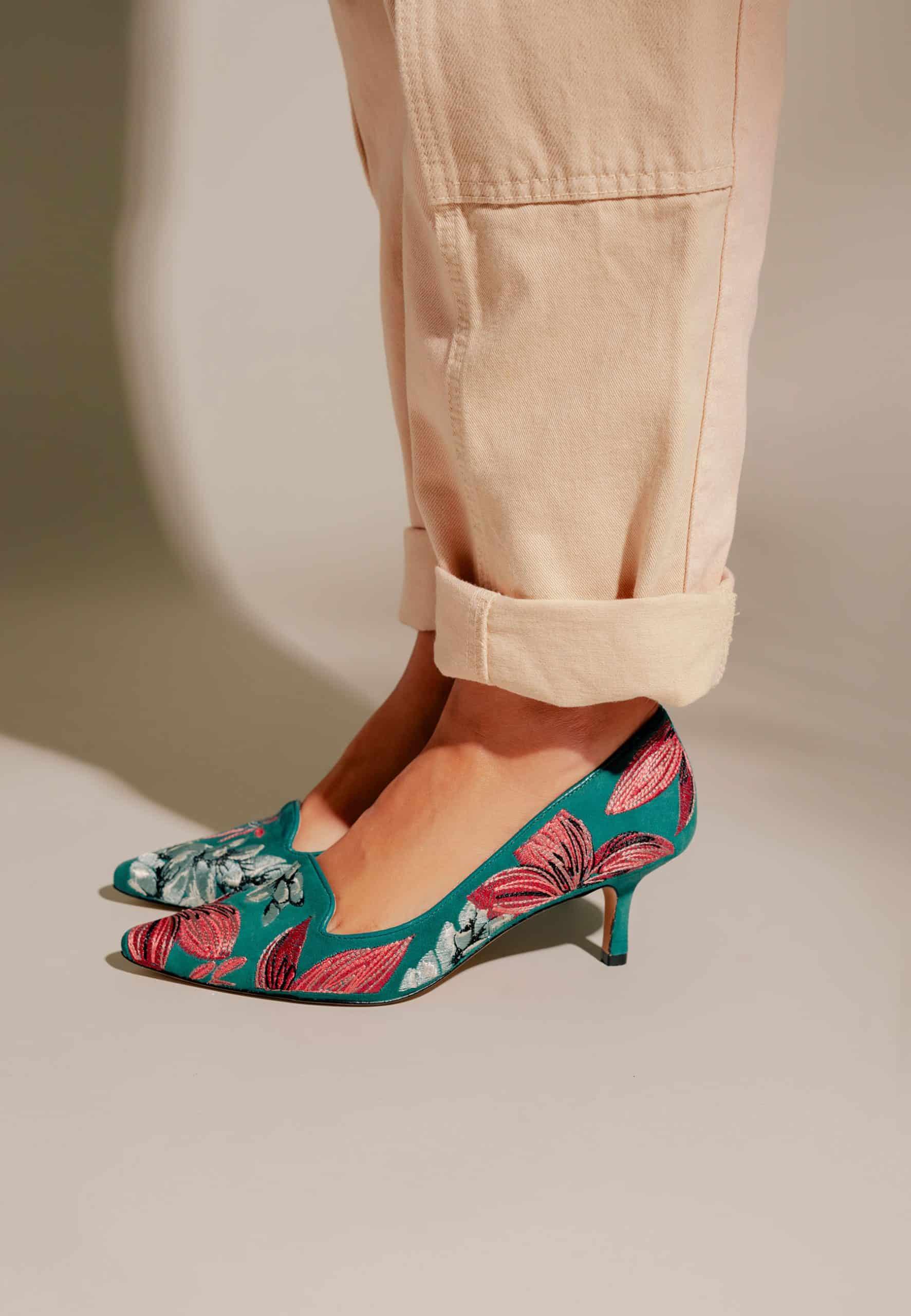 Teal shoes with pink floral pattern worn with beige pants on a neutral background