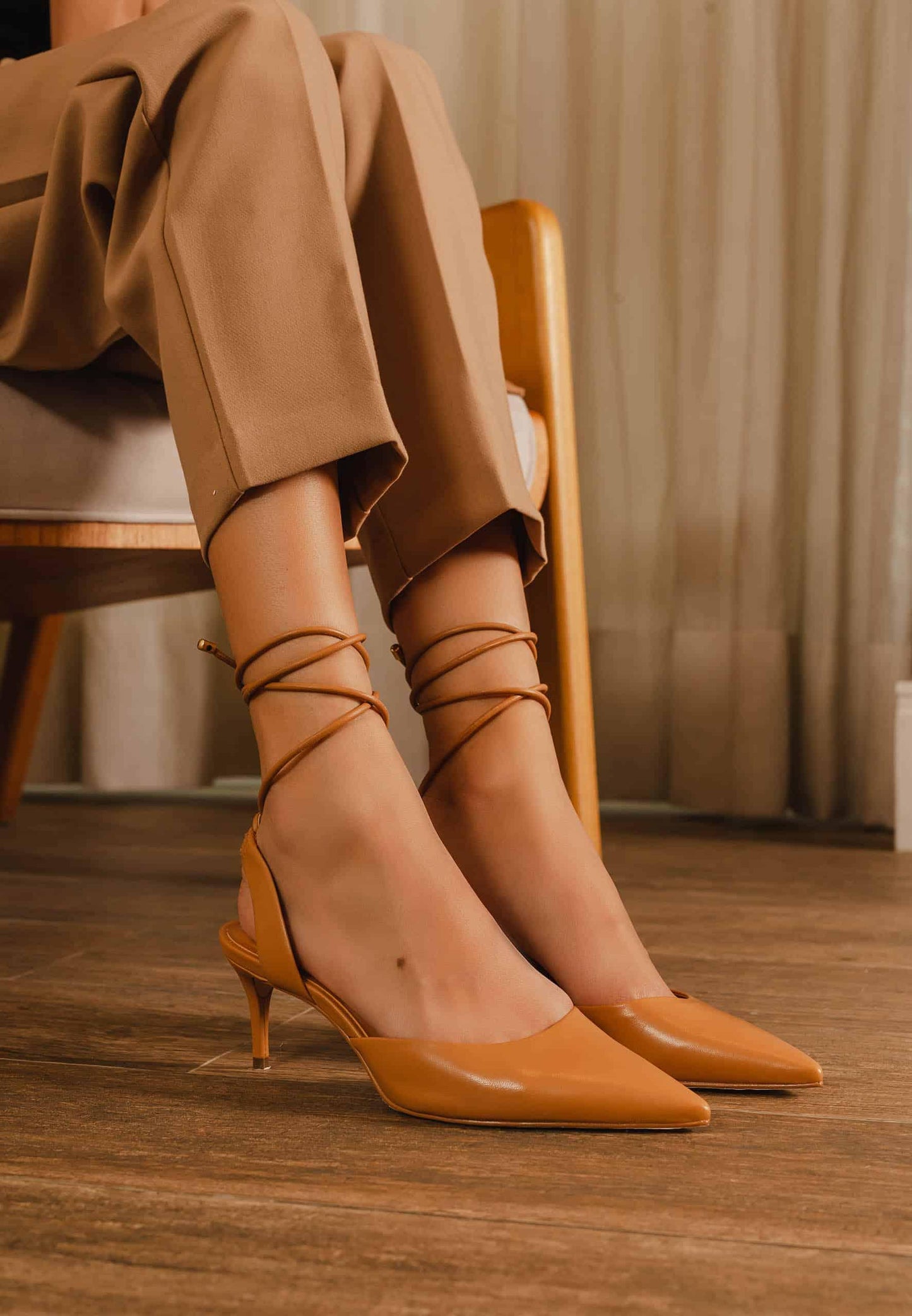 Person wearing brown high-heeled shoes and beige pants sitting on a chair.