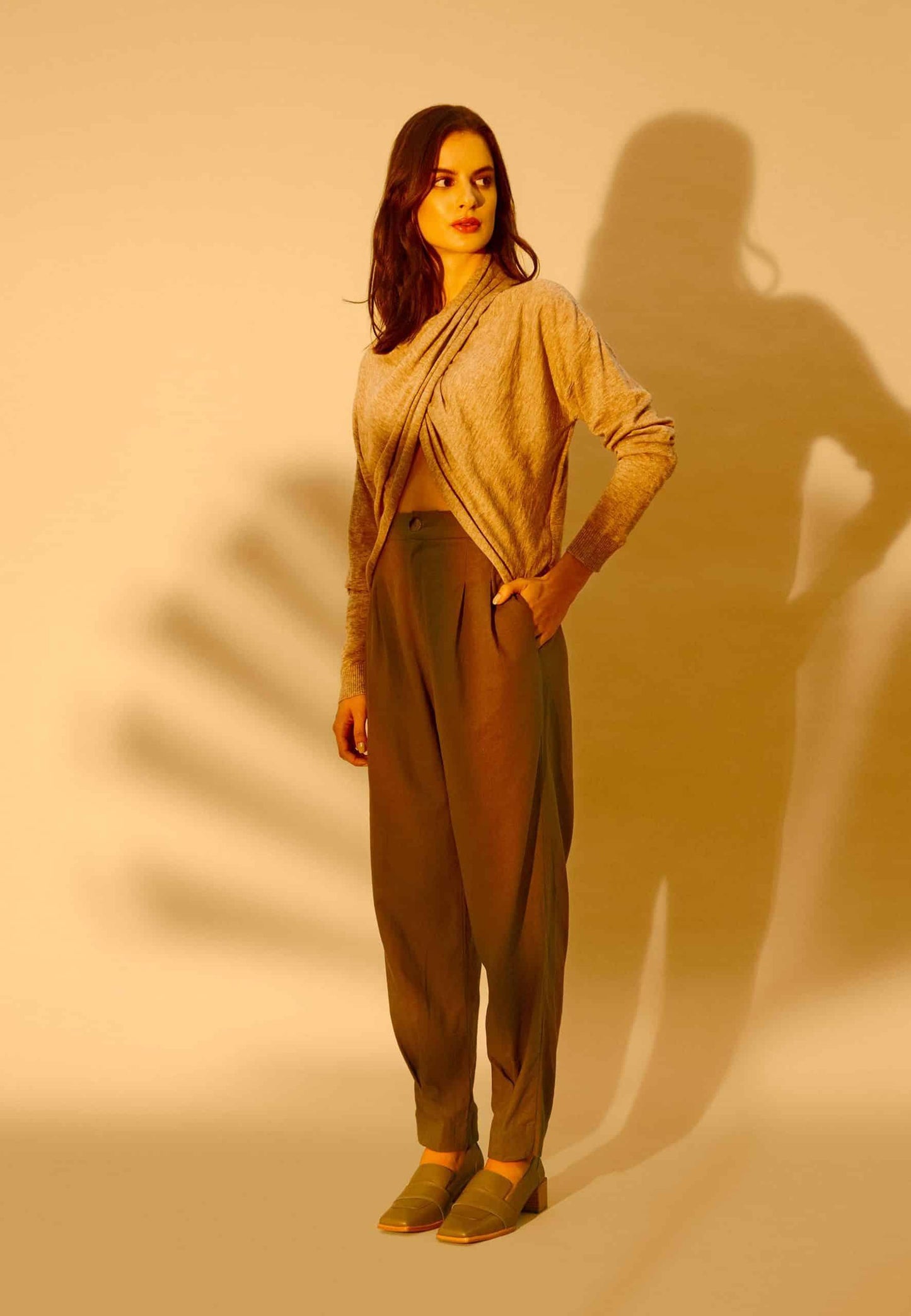 Woman wearing a beige outfit with a draped top and high-waisted pants against a beige background