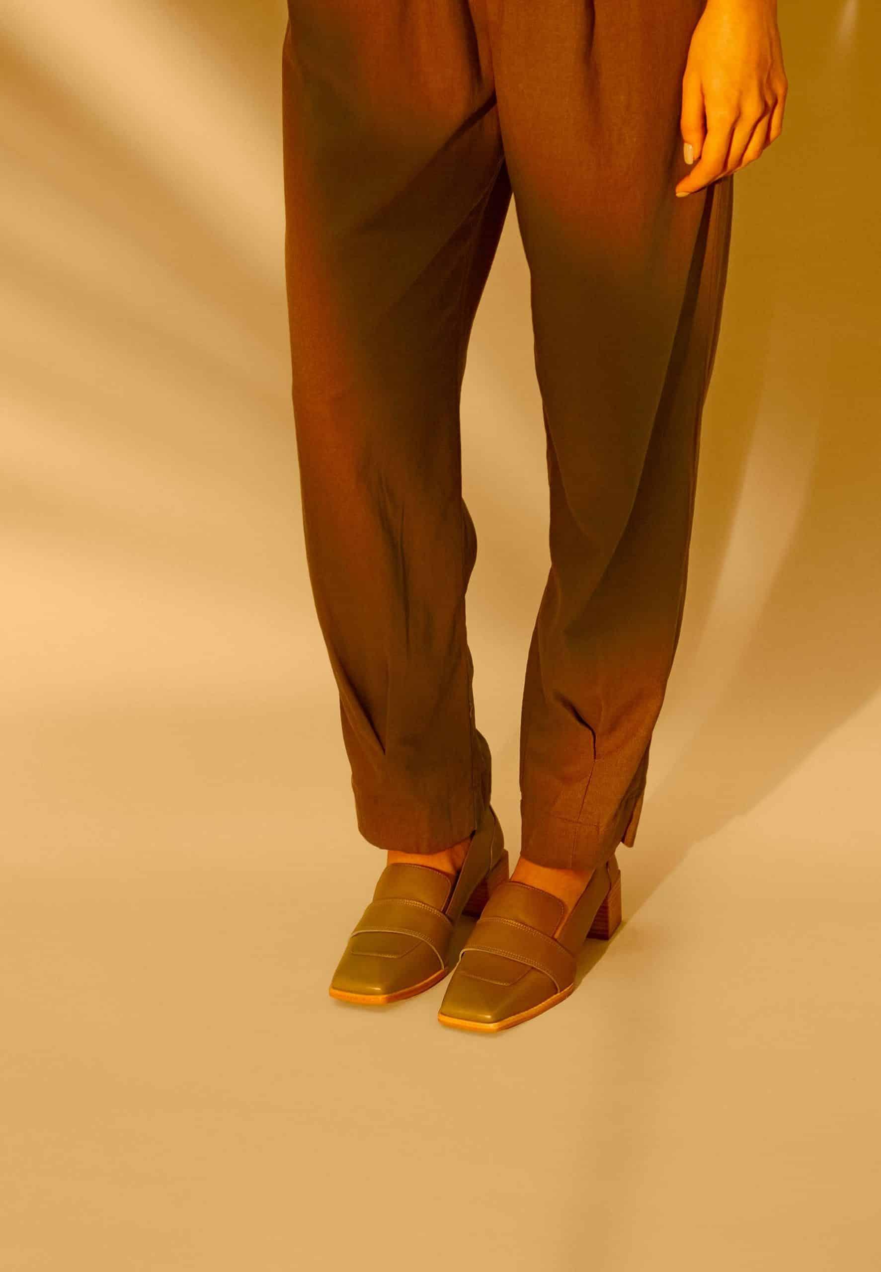 Person wearing brown pants and mustard shoes on a beige background