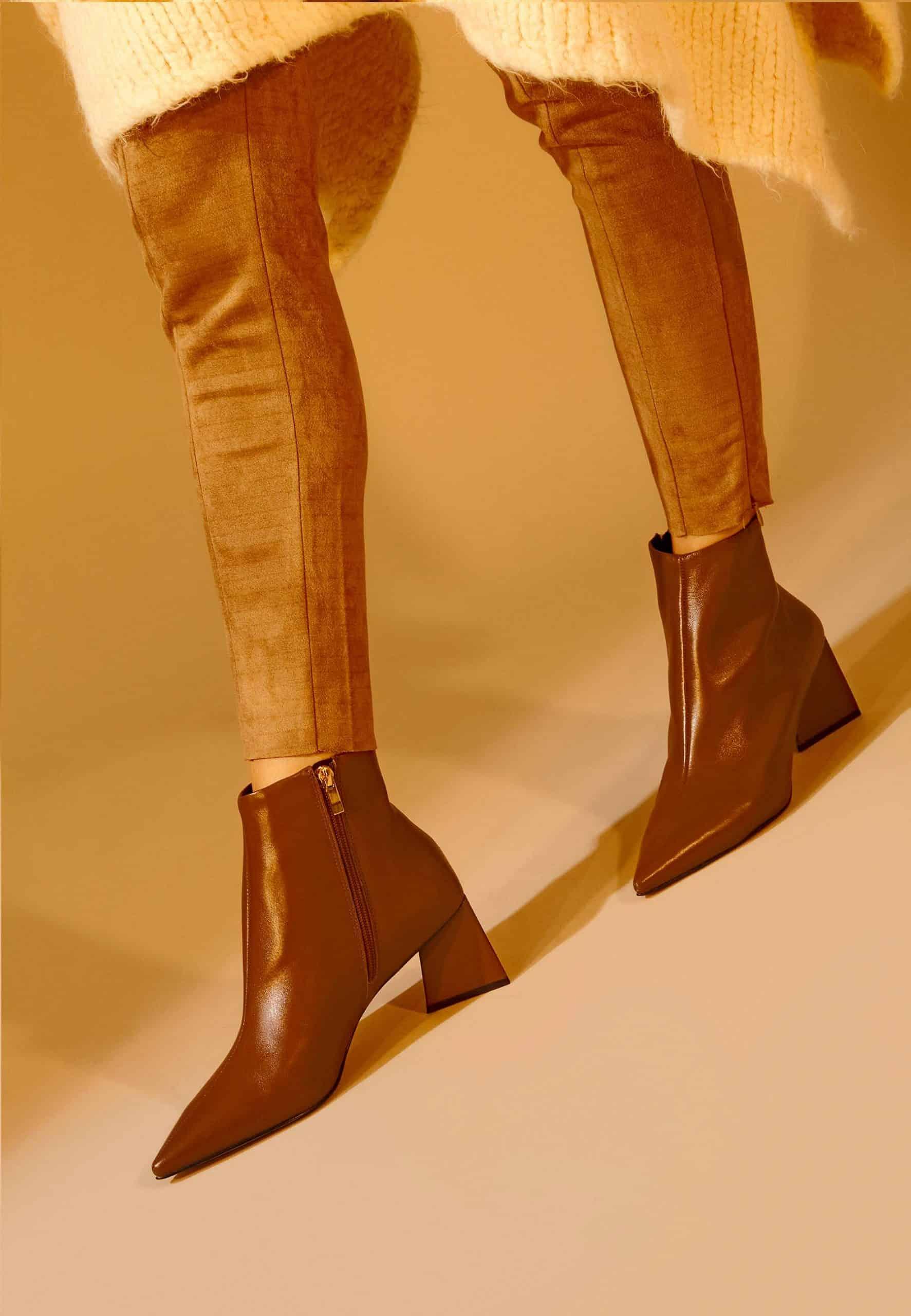 Brown leather boots worn with beige pants on a beige background